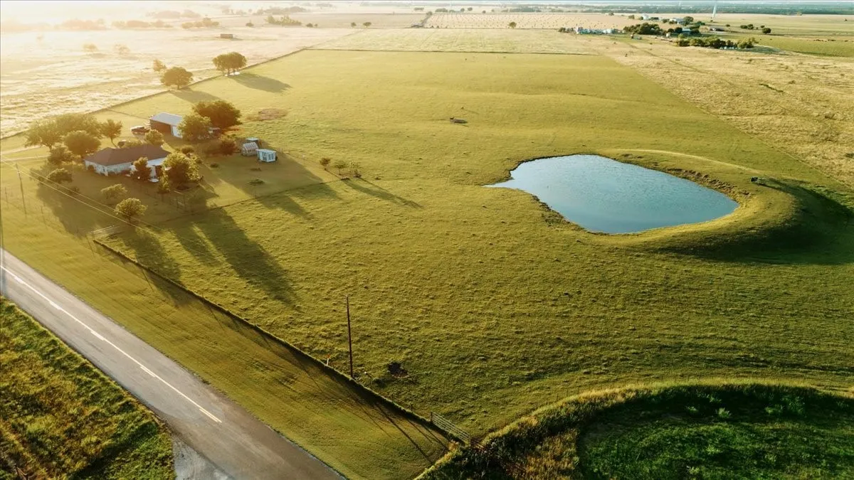 Expansive rural property featuring a main residence, multiple outbuildings, a natural pond, and a paved road frontage