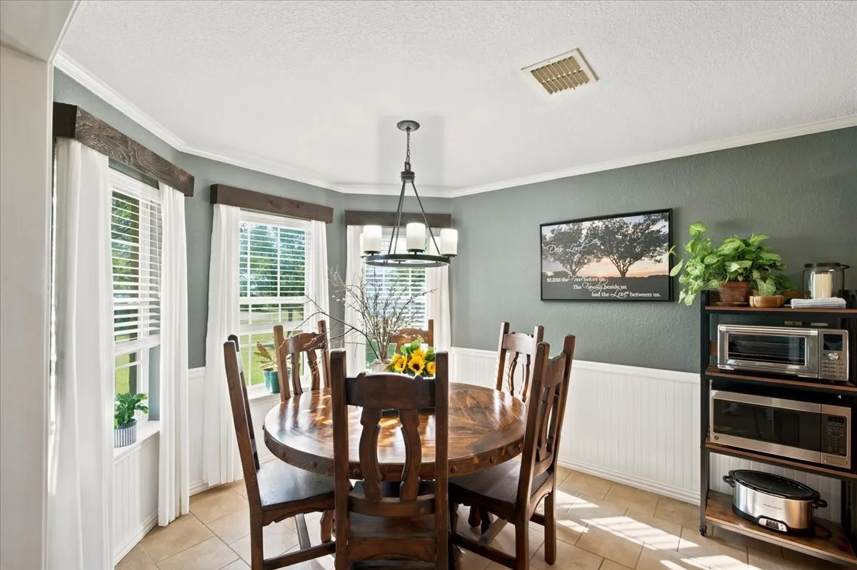 Dining area featuring a bay window with natural wood valances, white blinds, and white curtains