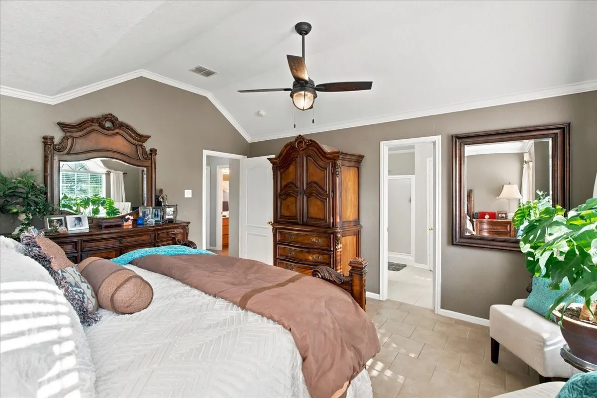 Vaulted ceiling with crown molding, ceiling fan with integrated lighting, and tile flooring