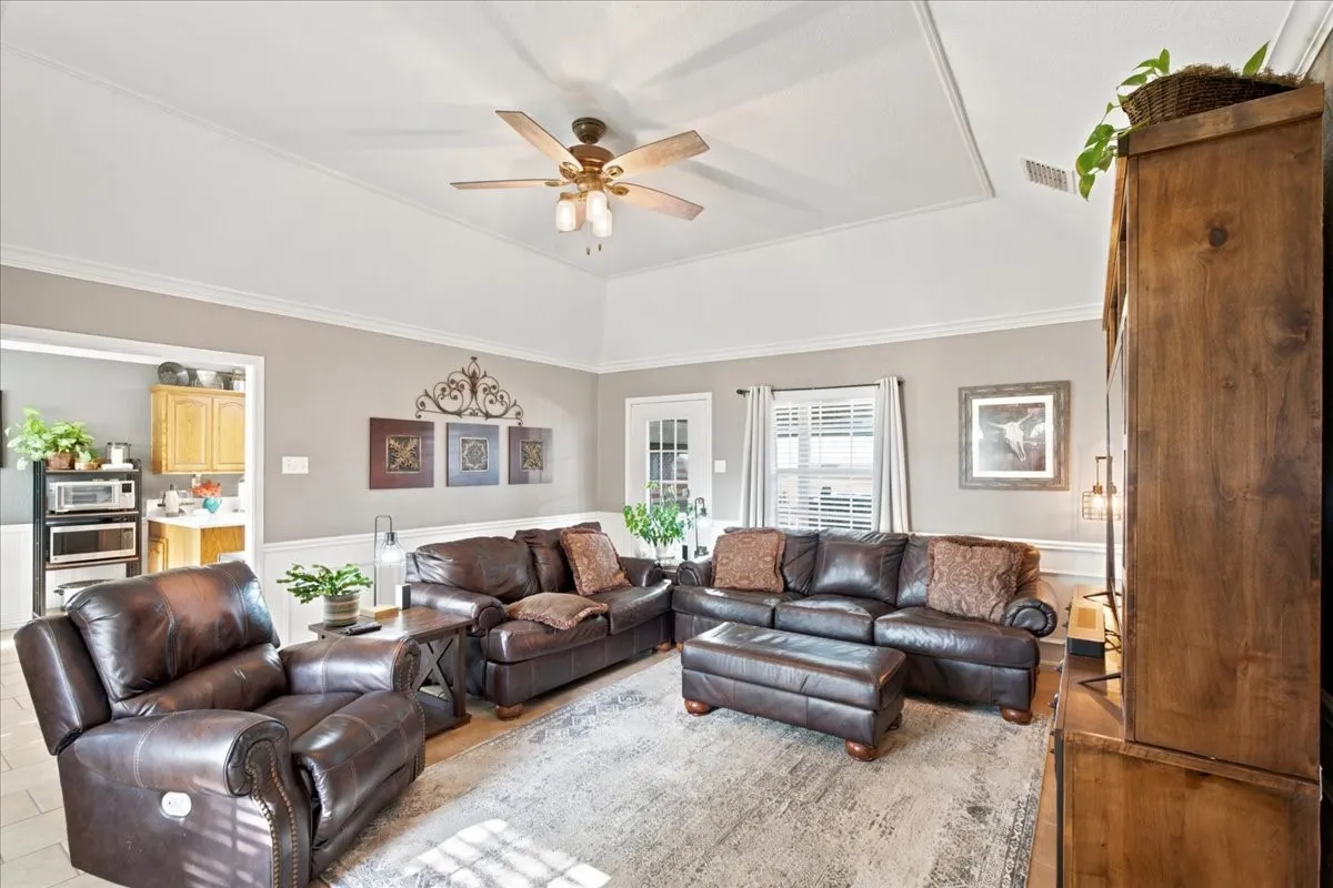 Living area featuring a tray ceiling with crown molding, a ceiling fan with integrated lighting, and neutral wall tones with wainscoting