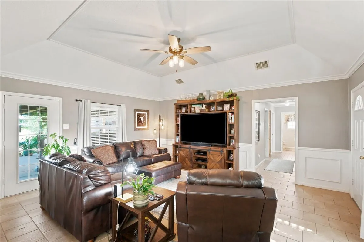 Spacious living area featuring a tray ceiling, crown molding, chair rail molding, and tile flooring