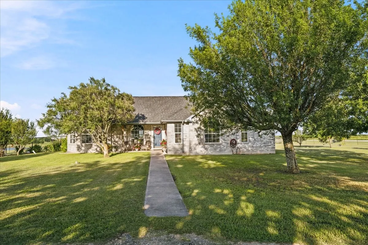 Stone-clad residence featuring a gabled roofline, concrete walkway, and expansive front lawn with mature trees