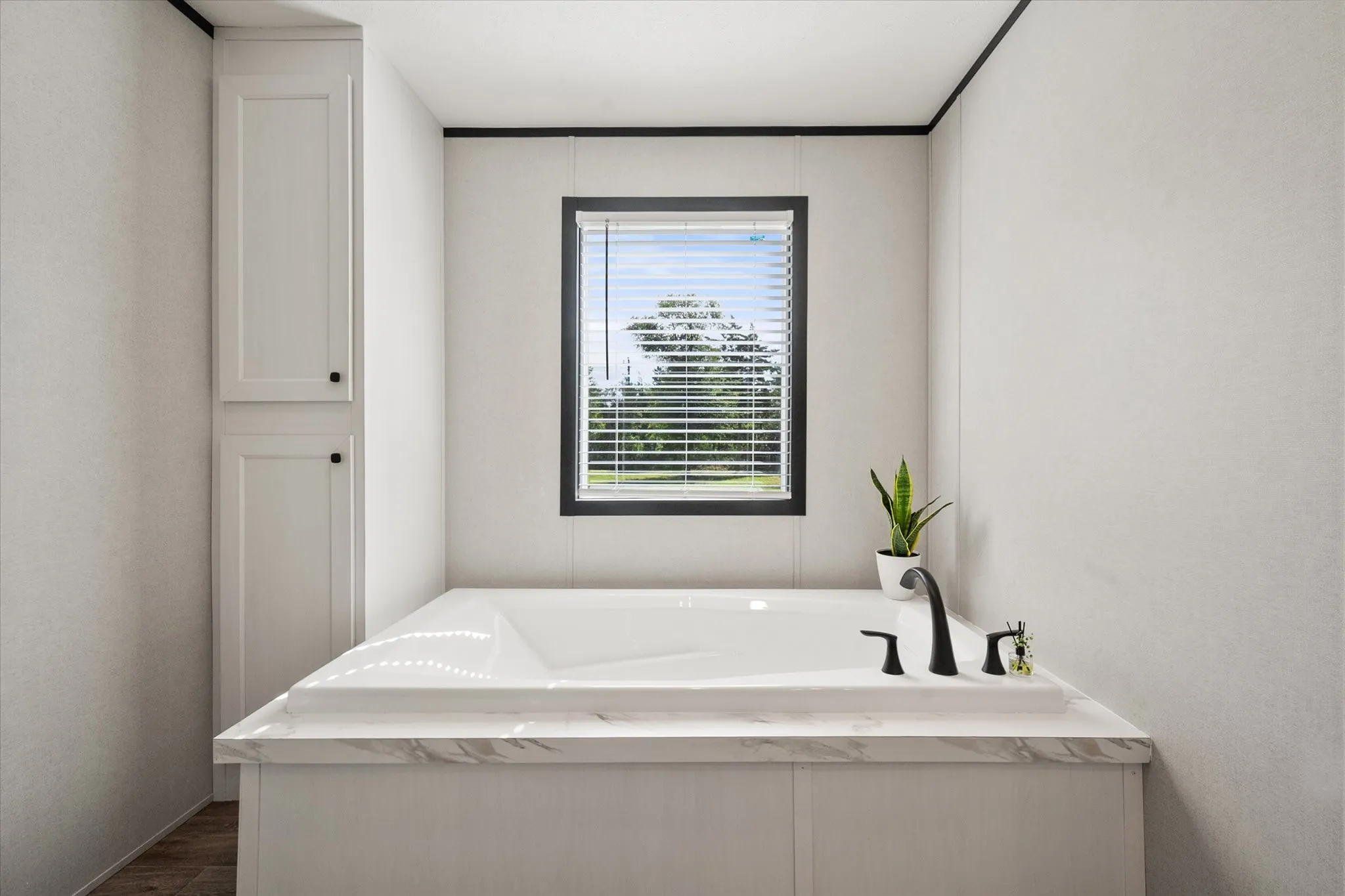 Soaking tub with black fixtures, and a window with blinds