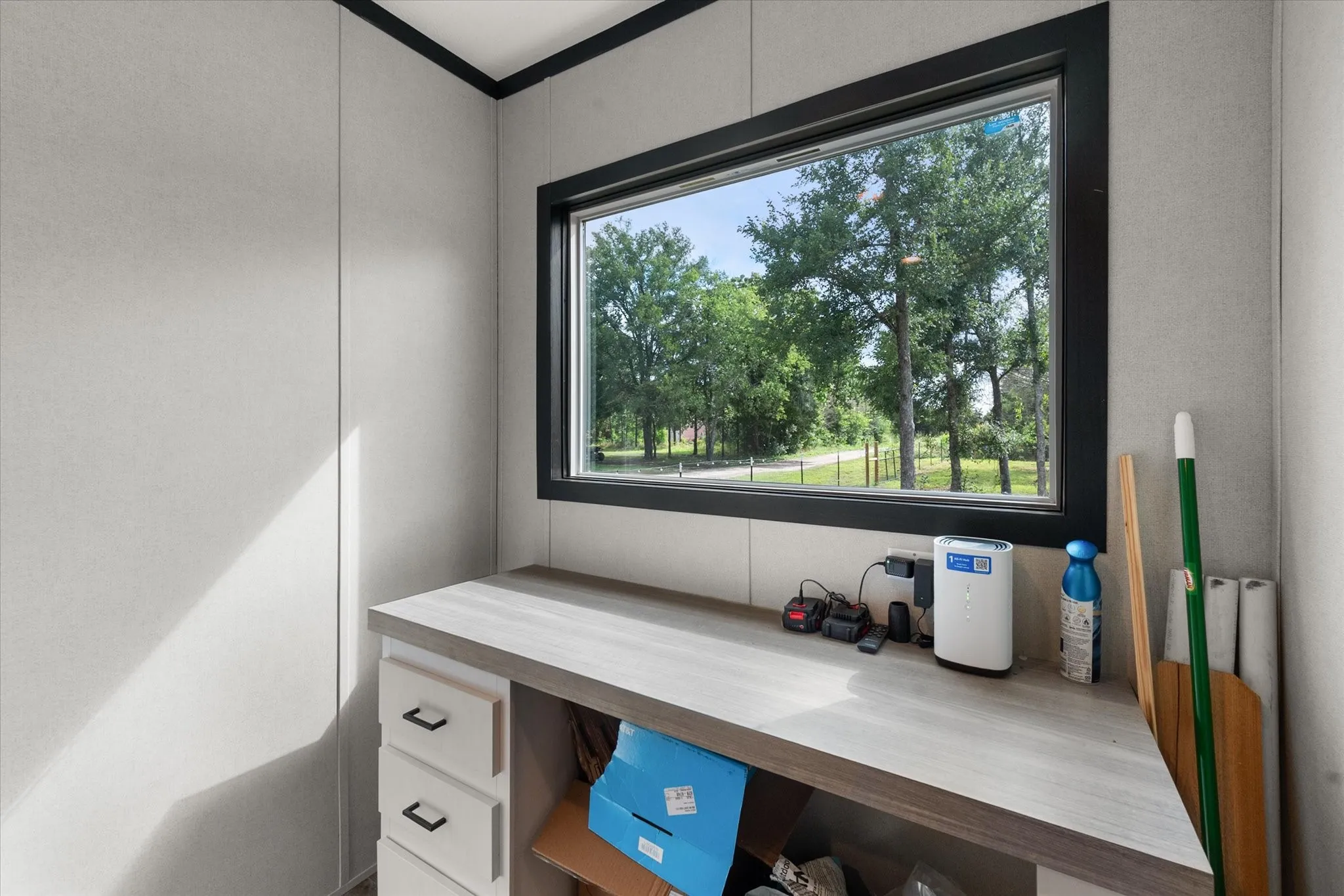 Built-in desk featuring a light wood-finish countertop, white cabinetry with dark hardware, and a large horizontal window