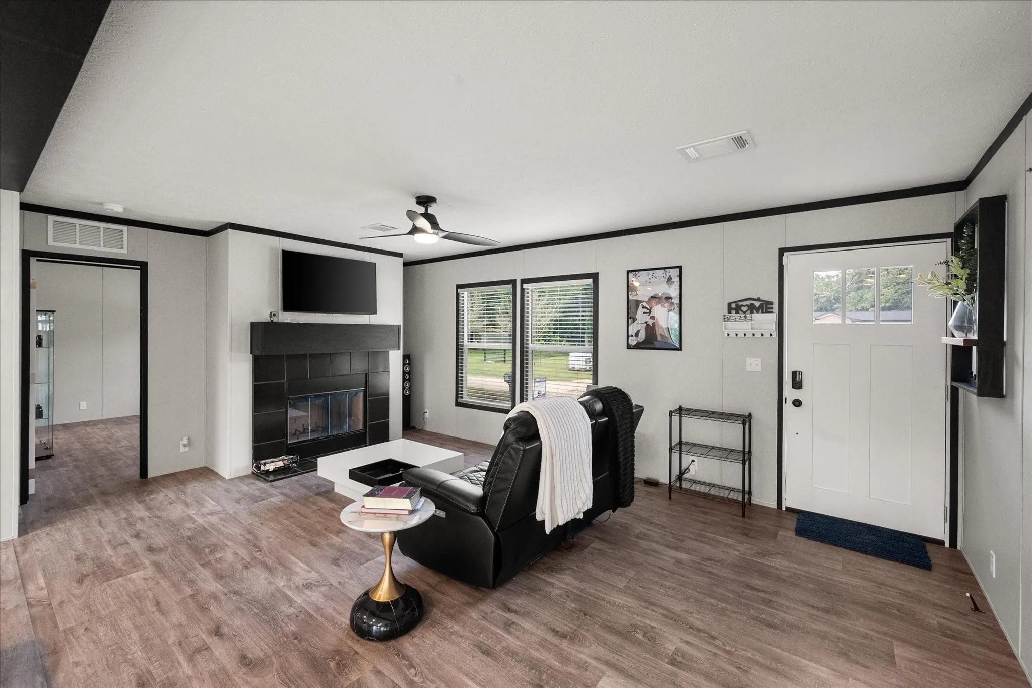 Spacious living area featuring wood-finish flooring, a black tiled fireplace with a mantel, and a multi-pane front door.