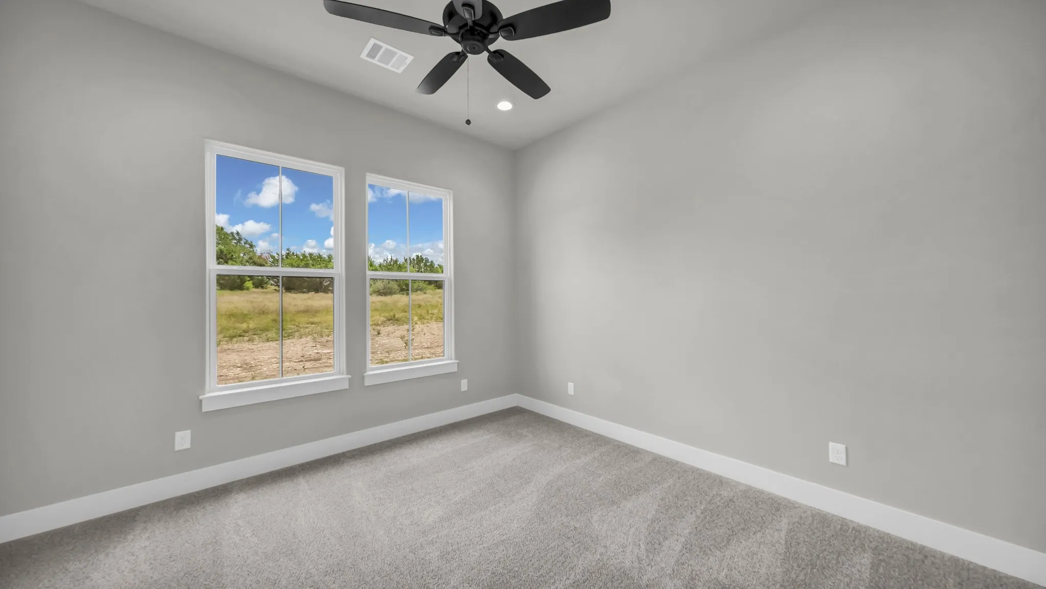 Spacious room featuring two large windows, light gray wall paint, and gray carpet flooring
