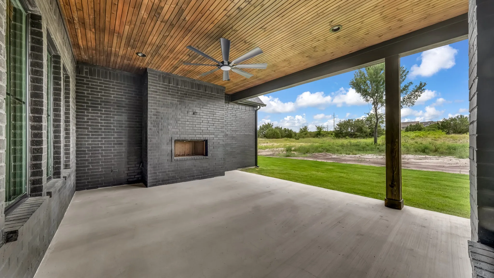 Covered patio with a wood-finish ceiling, built-in fireplace, and a ceiling fan