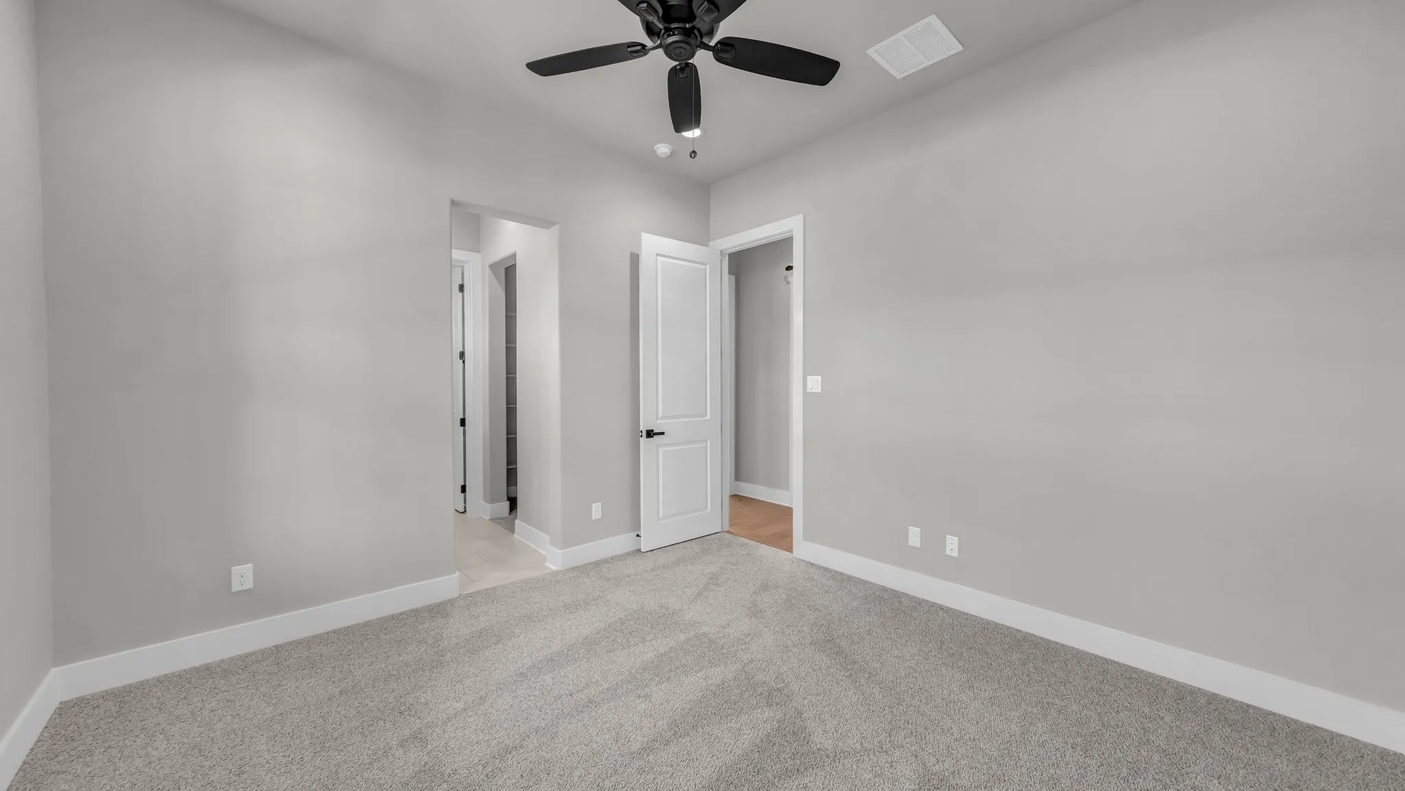 Carpeted room featuring a ceiling fan with black blades, vaulted ceiling, and white baseboards