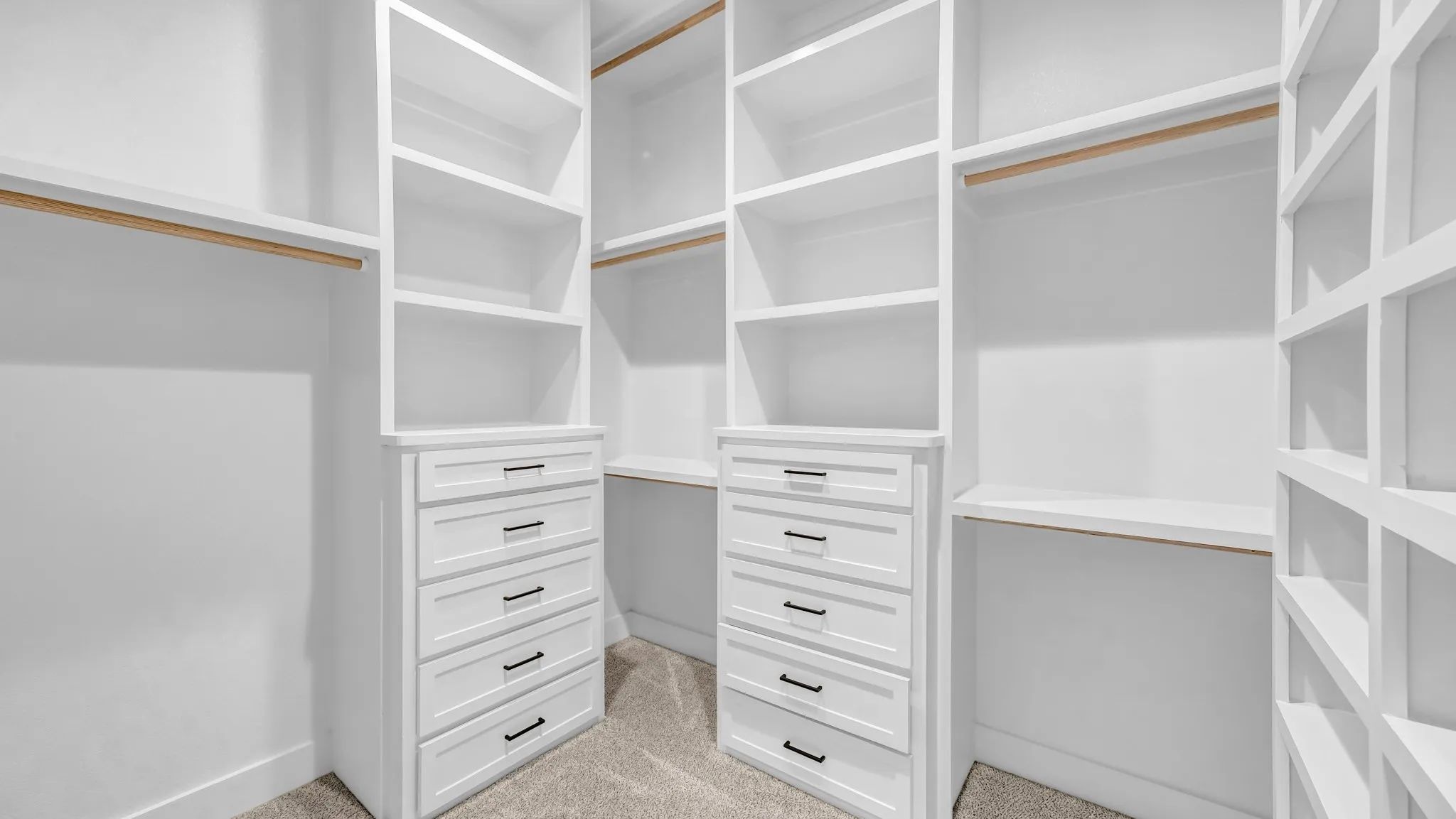 Custom built-in closet system featuring white cabinetry, multiple shelving units, integrated dresser drawers with black hardware, hanging rods, and neutral-toned carpeting