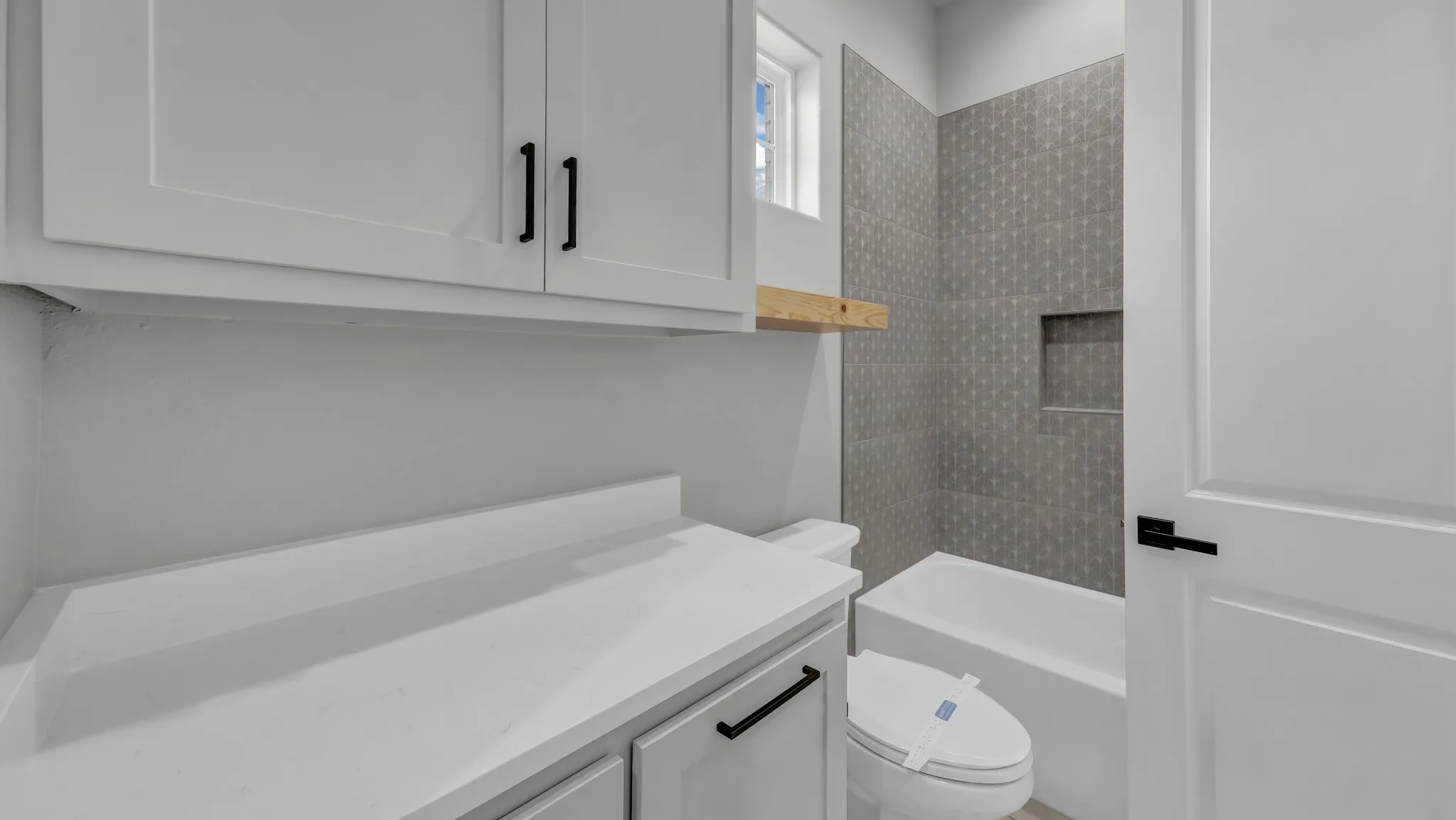 Bathroom featuring a white bathtub with a tiled surround, an integrated shower niche, and a window