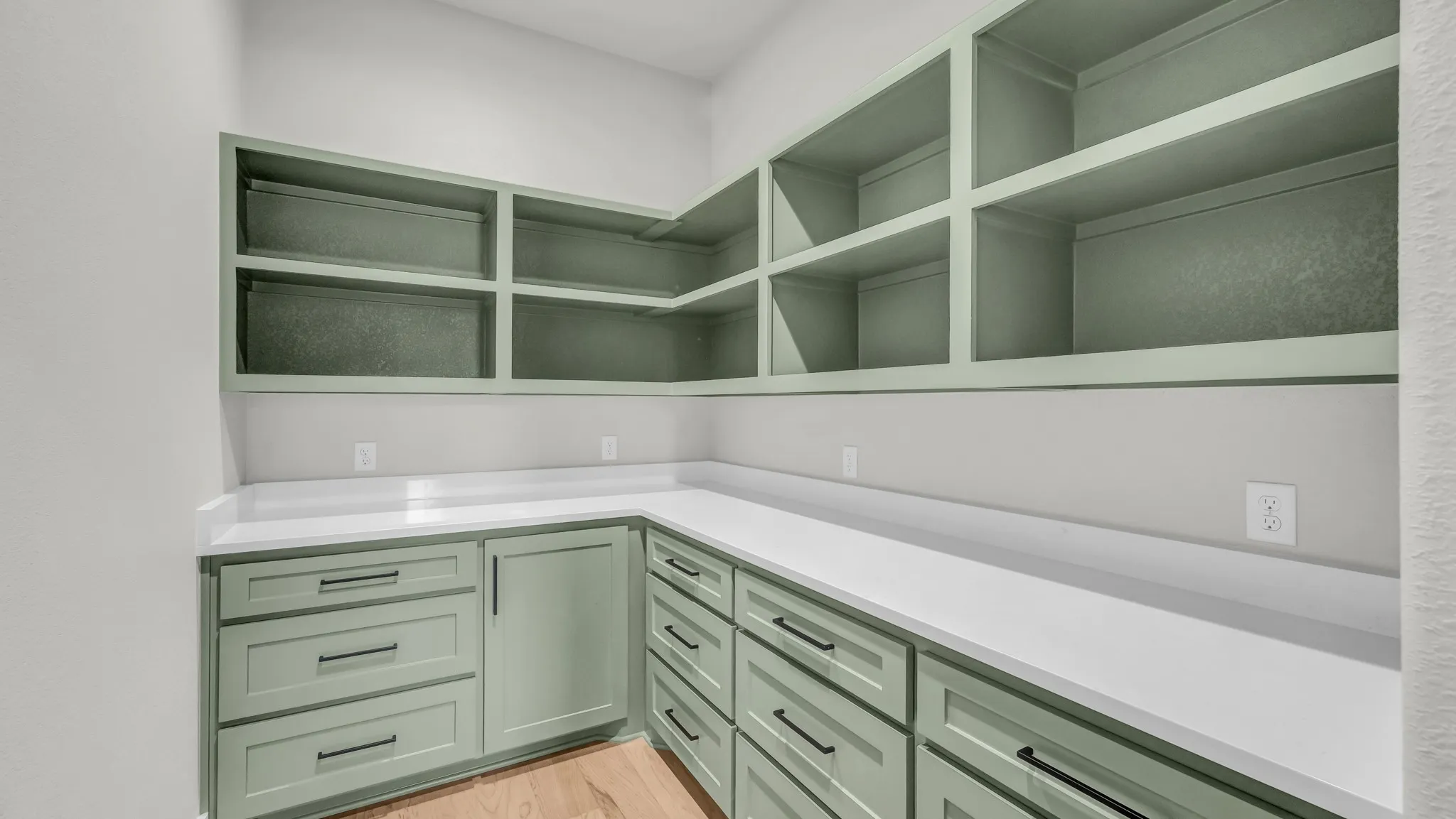 Built-in open shelving and lower cabinetry in a light green finish, complemented by a white countertop and wood-finish flooring