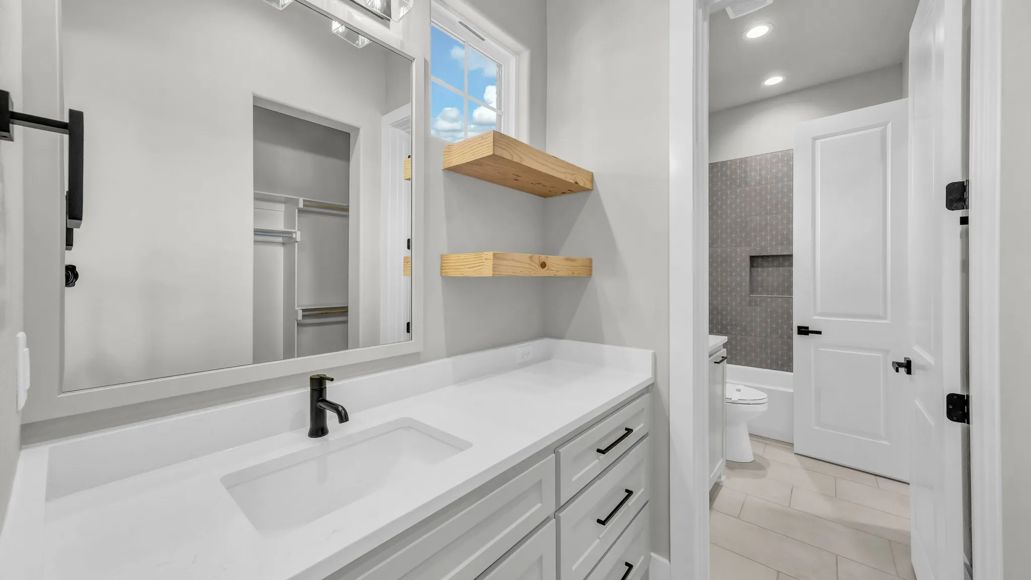 Bathroom featuring a white vanity with an integrated sink and matte black faucet, a large framed mirror, and two floating wood shelves