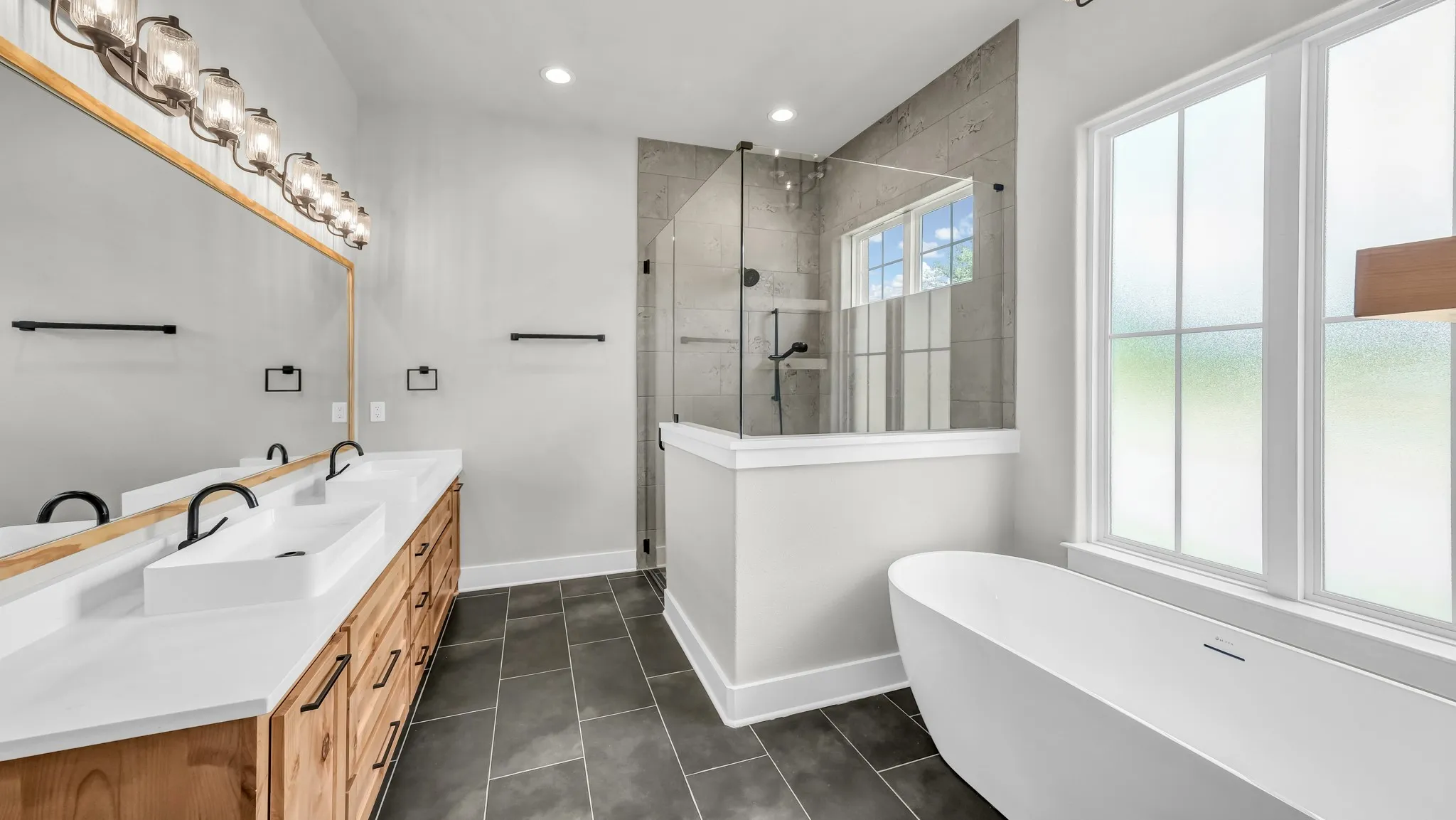 Modern bathroom featuring a freestanding soaking tub, a spacious glass-enclosed shower with tile surround, and a double vanity with rectangular vessel sinks