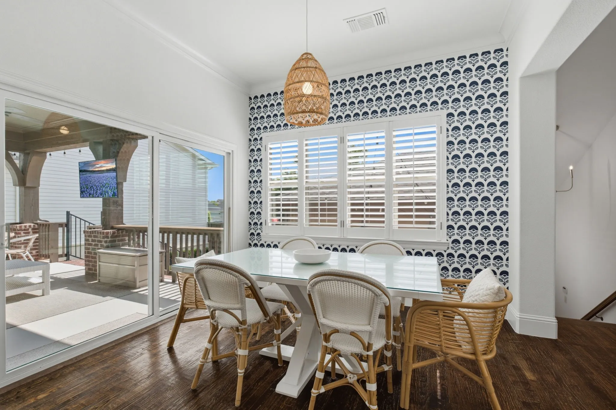 This bright and inviting sun-filled breakfast nook serves as the perfect casual dining space, featuring beautifully maintained shuttered windows that allow for plenty of natural light. The room includes a convenient sliding glass door that provides easy access to the large, expansive covered back porch, while a charming and sophisticated wallpaper accent wall adds a touch of unique character, perfectly highlighting the original craftsman charm of this lovely home.