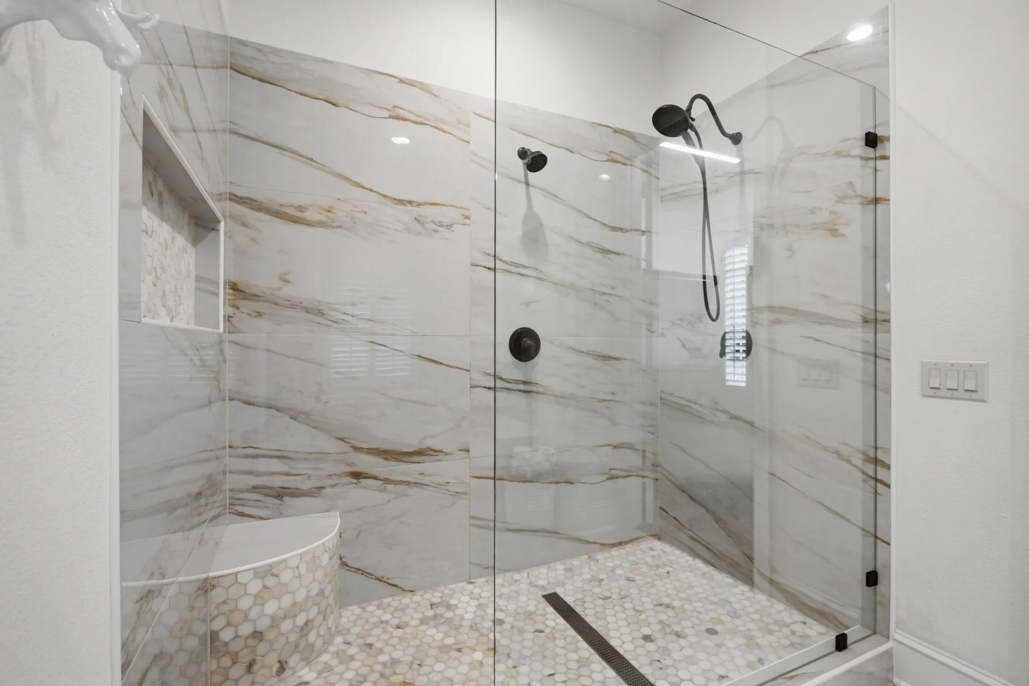 Luxury primary bathroom featuring a spacious walk-in shower with dual shower heads, a built-in bench seat, and a custom shampoo niche.