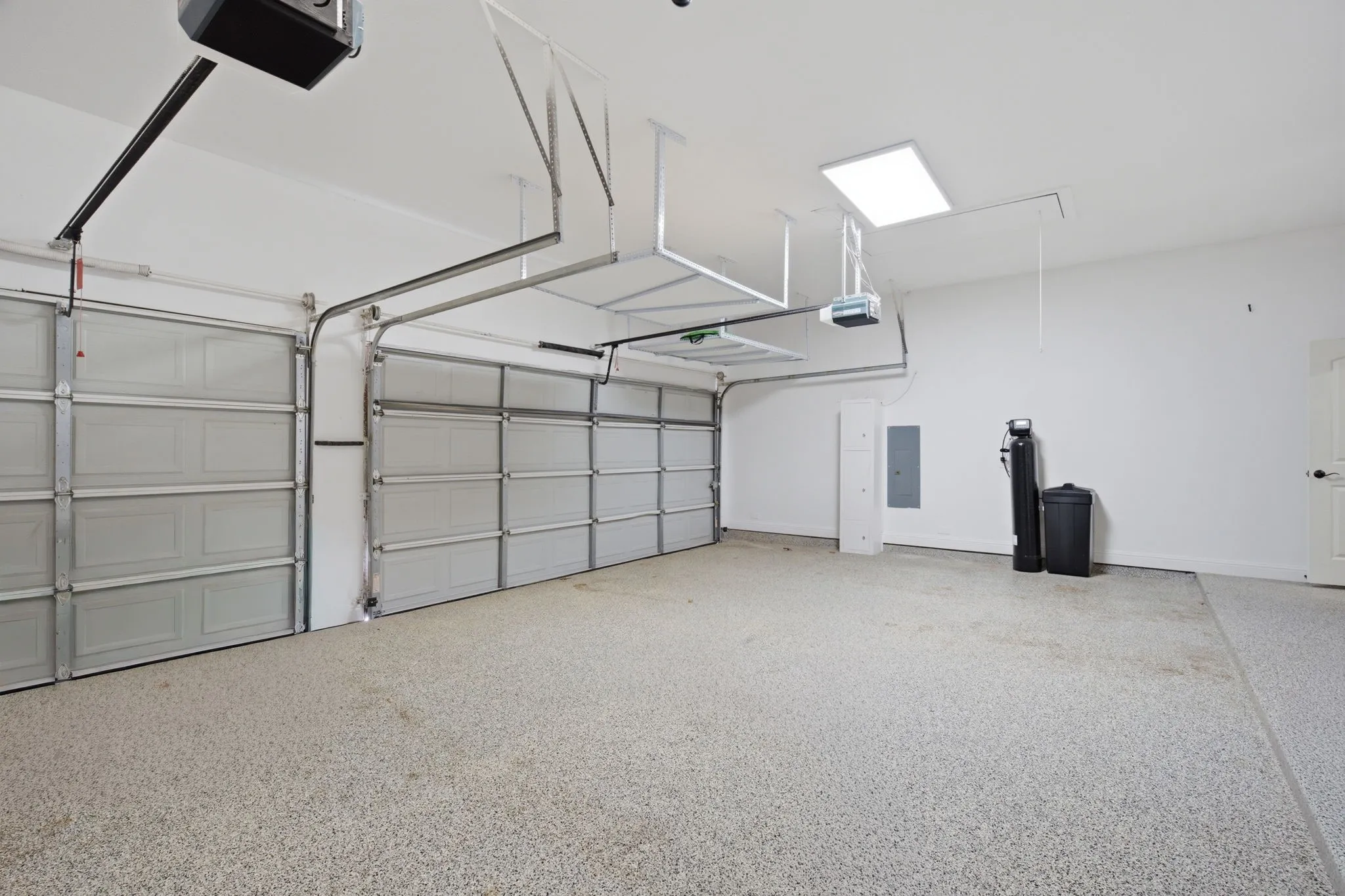 Spacious 3-car garage featuring a epoxy-coated floor,  extra-high ceilings equipped with integrated overhead storage racks, and a convenient, fully enclosed 6'10" x 6'9" storage closet located at the rear for optimal organization and functionality.
