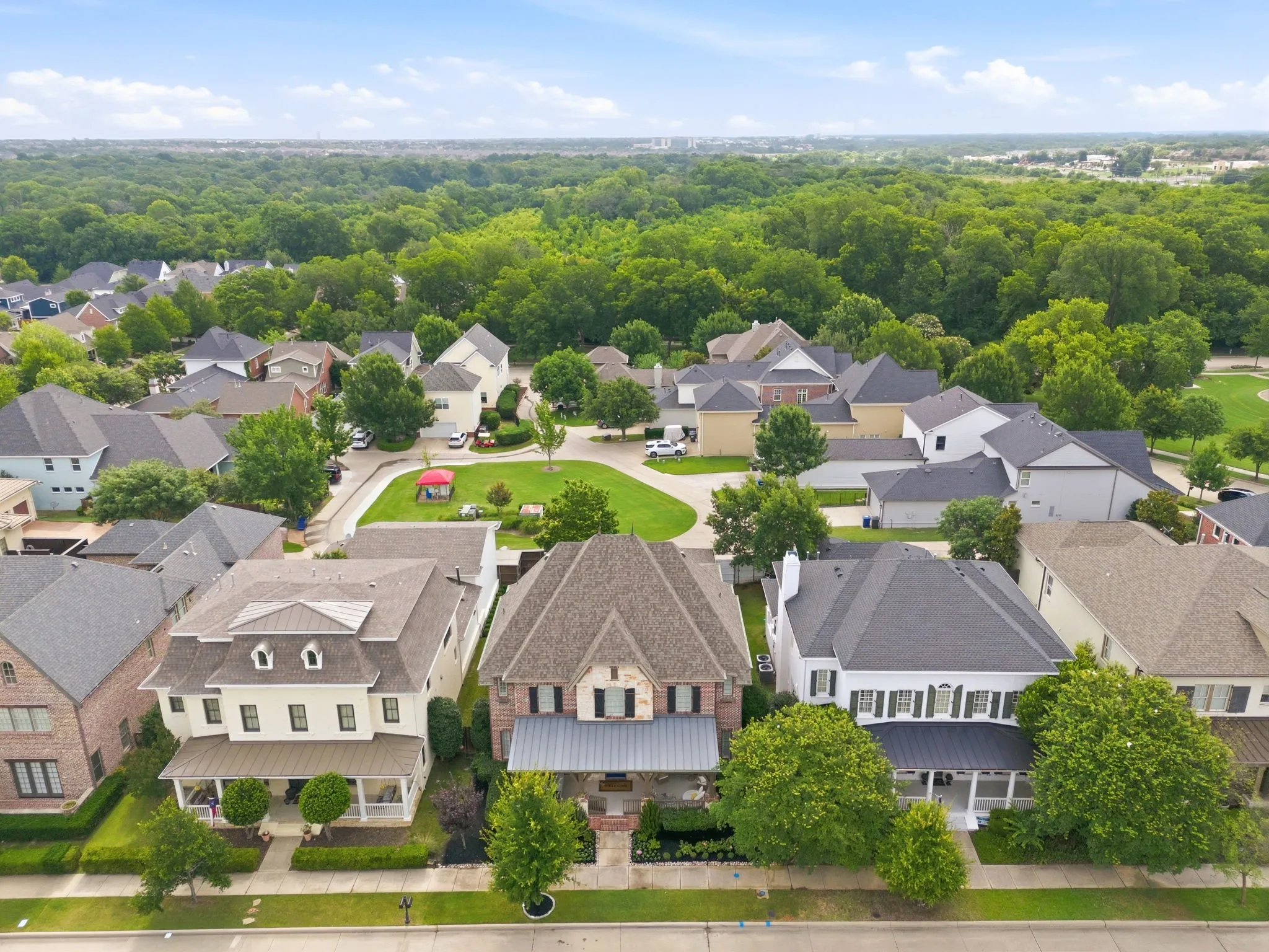 This stunning aerial view highlights the picturesque charm of this sought-after craftsman-style neighborhood, perfectly capturing the lush, mature trees that line the streets throughout the entire community. In the background, you can clearly see the expansive, well-maintained grassy park area situated directly behind the property, offering residents an ideal space for outdoor recreation and peaceful relaxation.