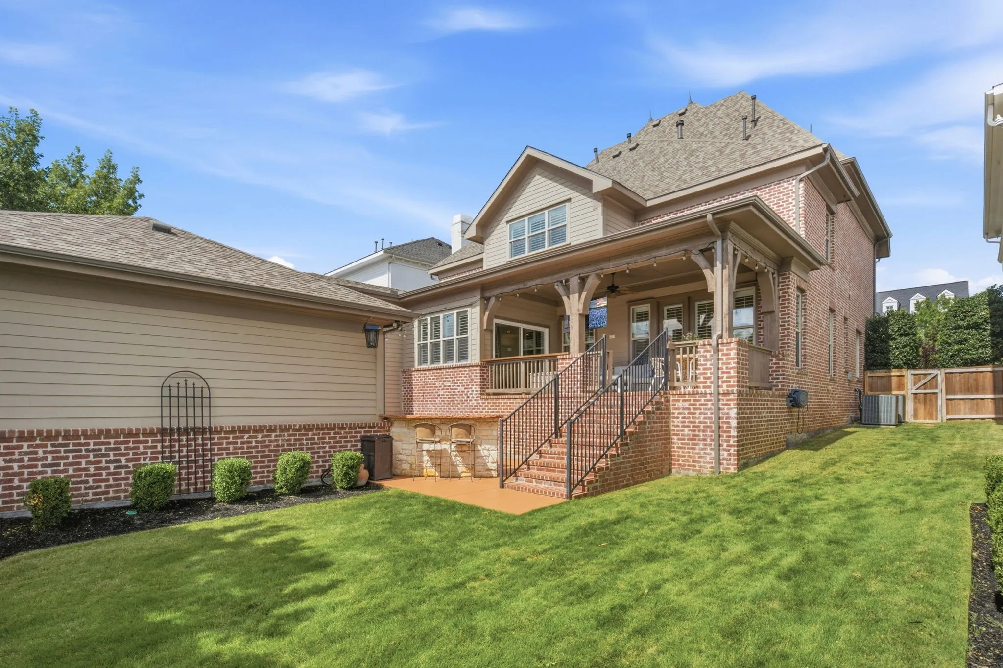 This meticulously landscaped backyard offers a serene outdoor retreat, featuring a wide, lush green grass area perfectly manicured for recreation and relaxation, elegantly bordered by a variety of vibrant, neatly trimmed bushes and ornamental shrubbery that provide both privacy and a sophisticated aesthetic appeal.
