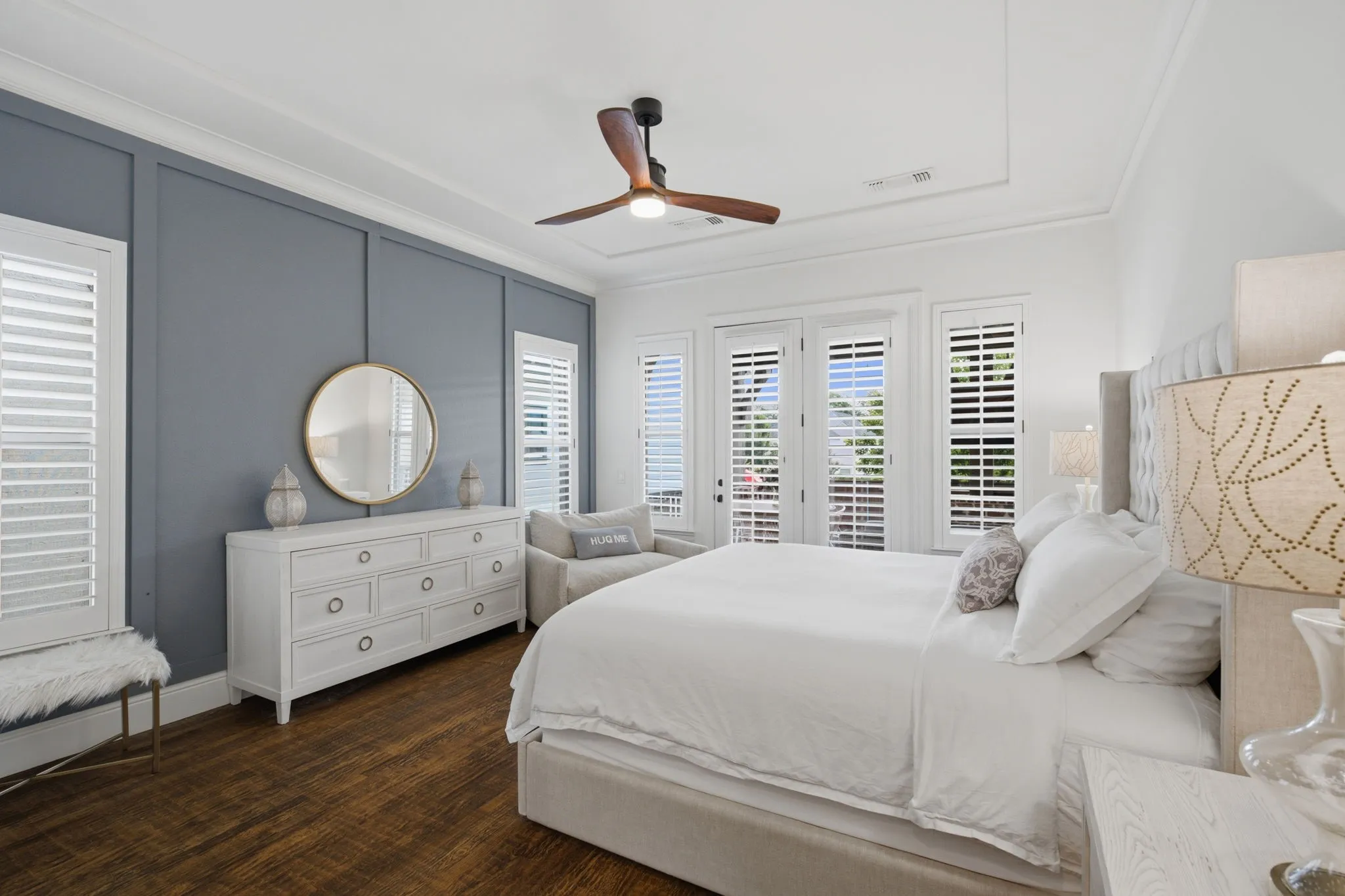 The primary bedroom is a sophisticated retreat, highlighted by beautiful French doors that provide seamless access to the back patio. The windows and doors are dressed with elegant, high-quality shutters that add a polished look while allowing for adjustable natural light. The room is grounded by rich, warm hardwood flooring throughout and features a stunning, professionally painted accent wall that serves as a stylish focal point for the space.