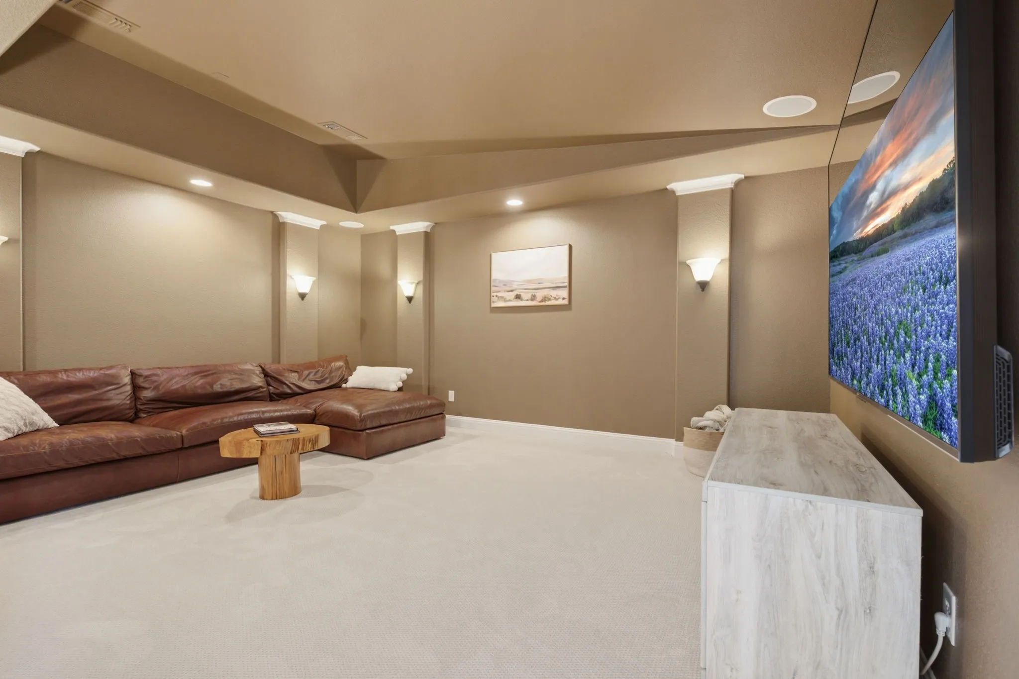 This spacious and inviting media room serves as the perfect entertainment hub, highlighted by the soft, ambient glow of sophisticated wall sconces that add an elegant touch to the overall aesthetic of the space.