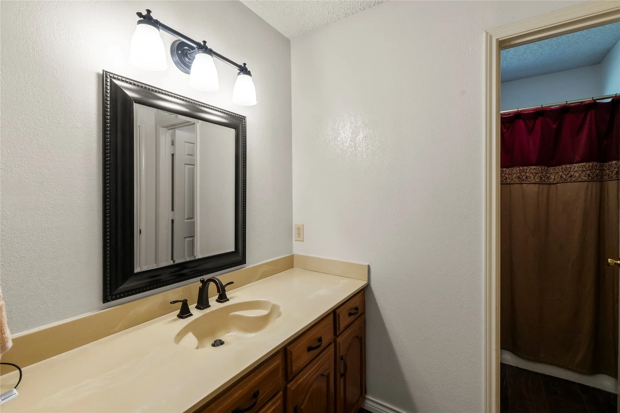 Bathroom vanity featuring a light-toned countertop with an integrated sink, dark wood-finish cabinetry, and a framed mirror