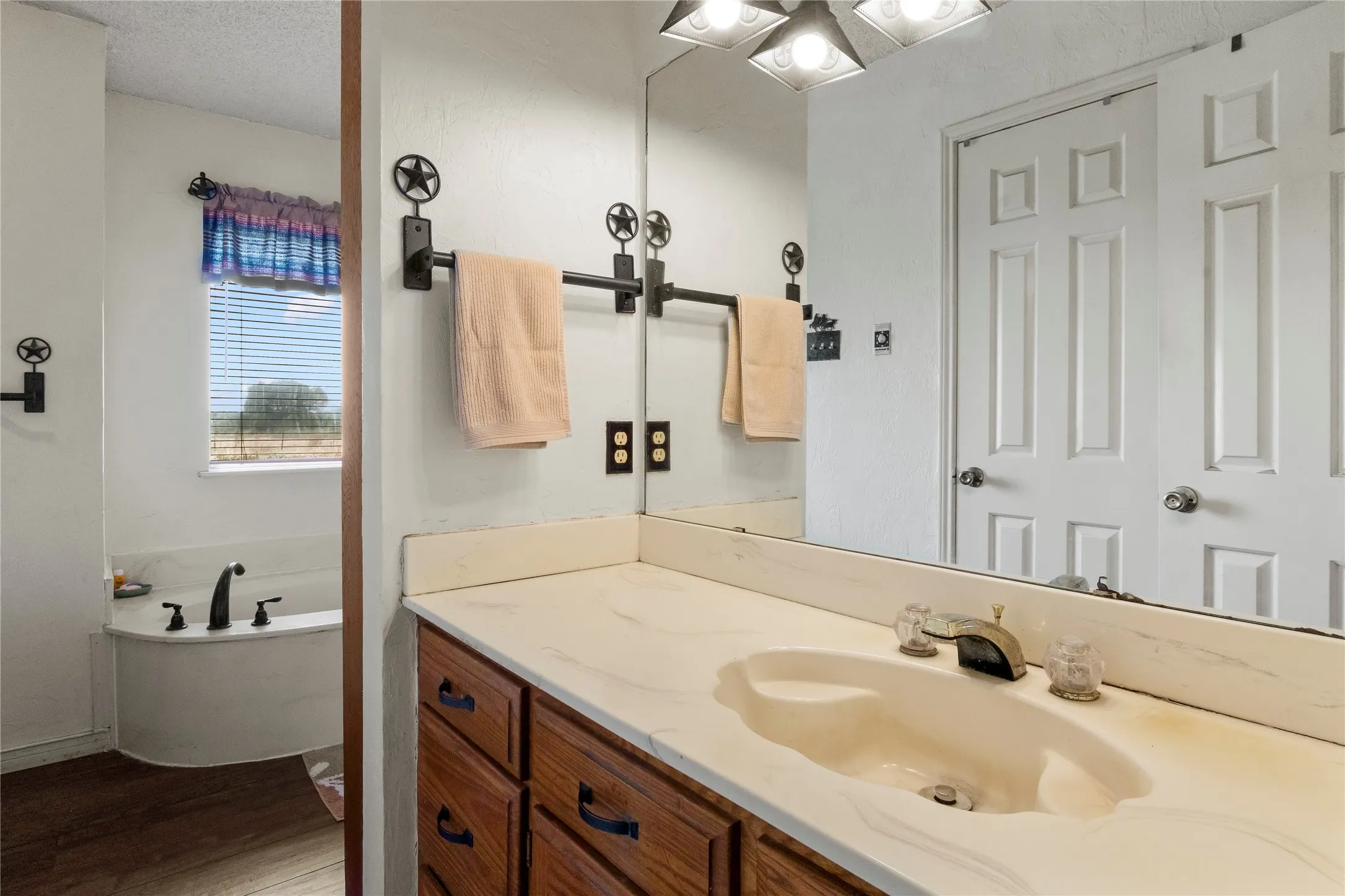 Bathroom vanity featuring wood cabinetry, a light-toned countertop with an integrated sink, and an expansive wall-mounted mirror