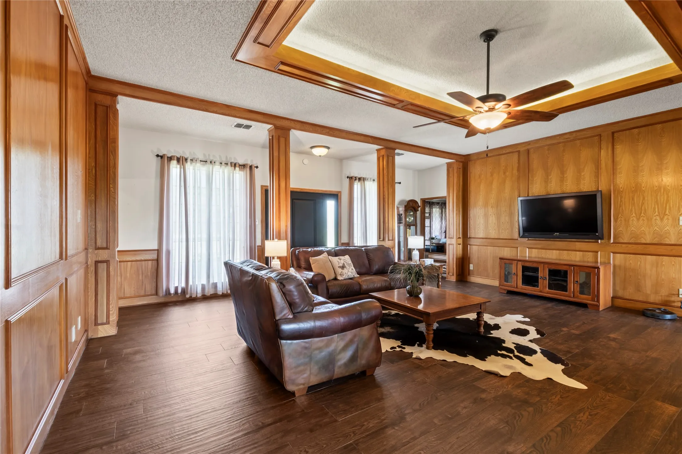 Spacious living area featuring extensive wood paneling, wood-finish flooring, and a coffered ceiling with integrated lighting