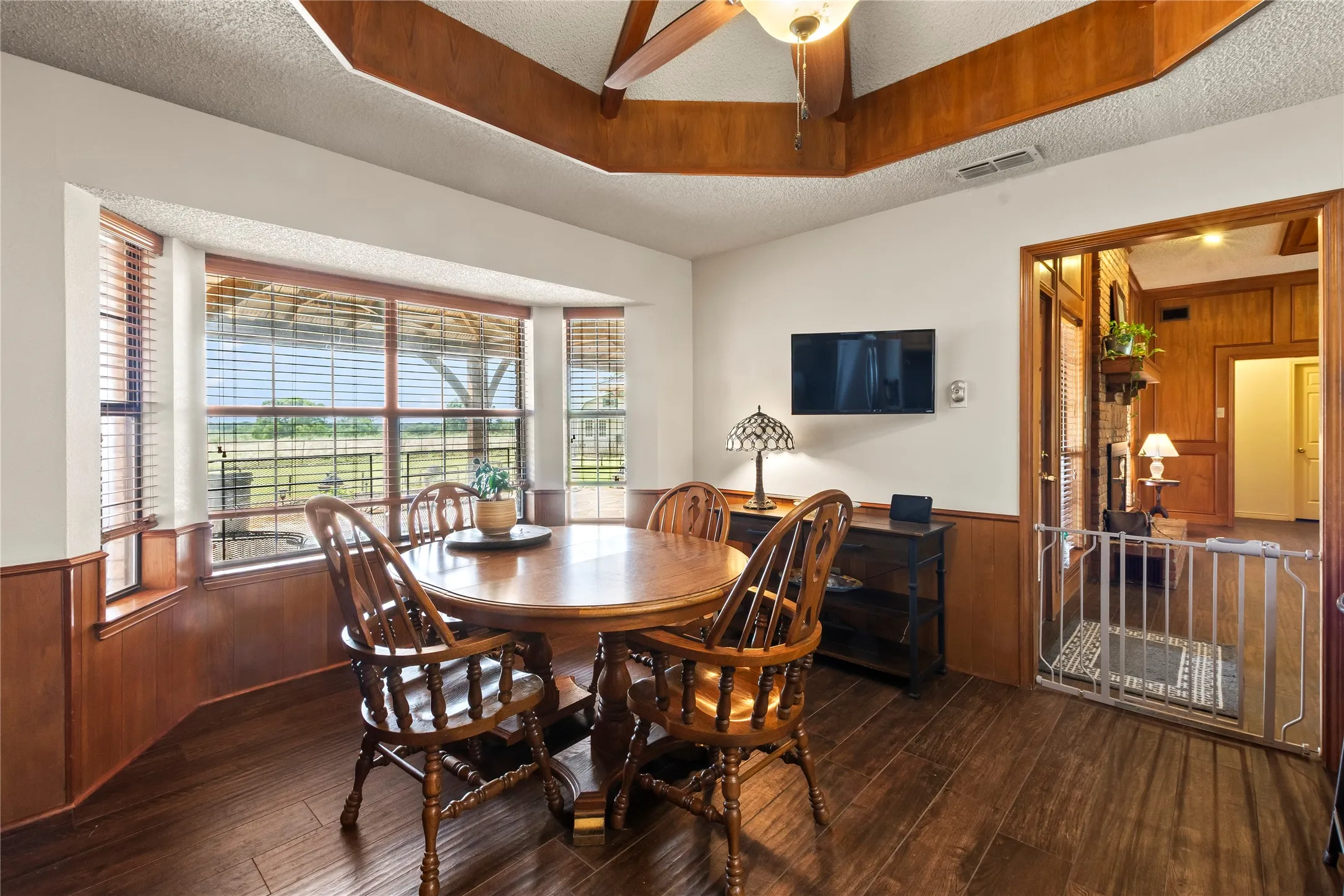 Dining area featuring dark wood-finish flooring, light wood wainscoting, and a bay window with blinds