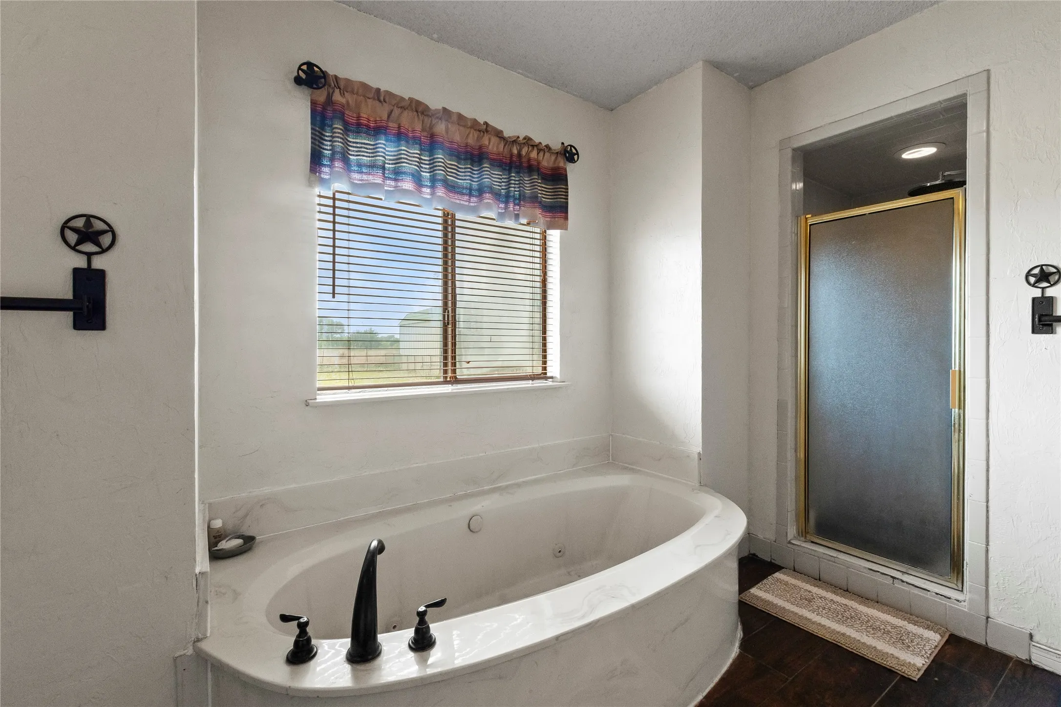 White soaking tub with dark bronze fixtures, integrated into a white surround