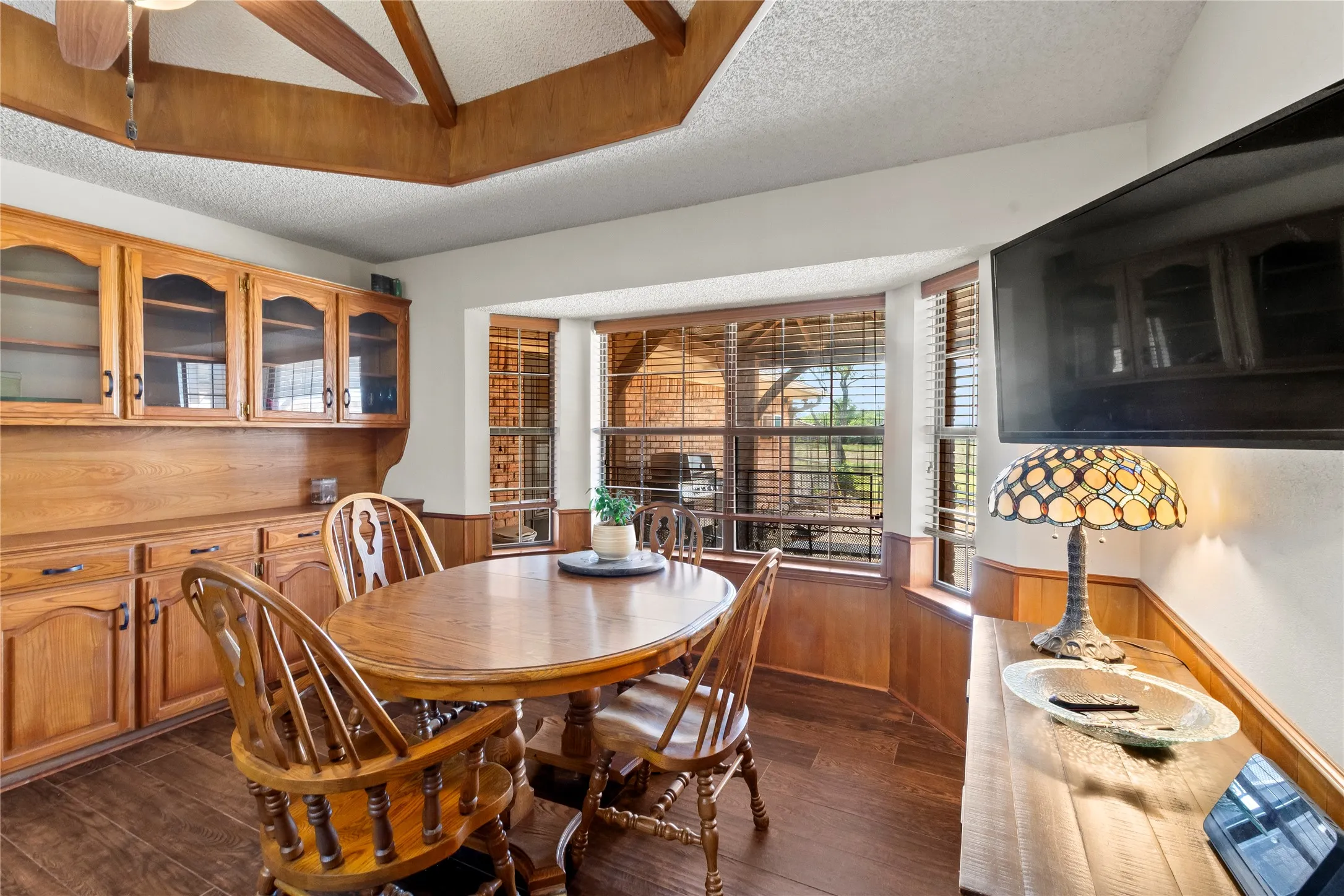 Dining space with a bay window, wood-finish flooring, and built-in cabinetry featuring glass inserts