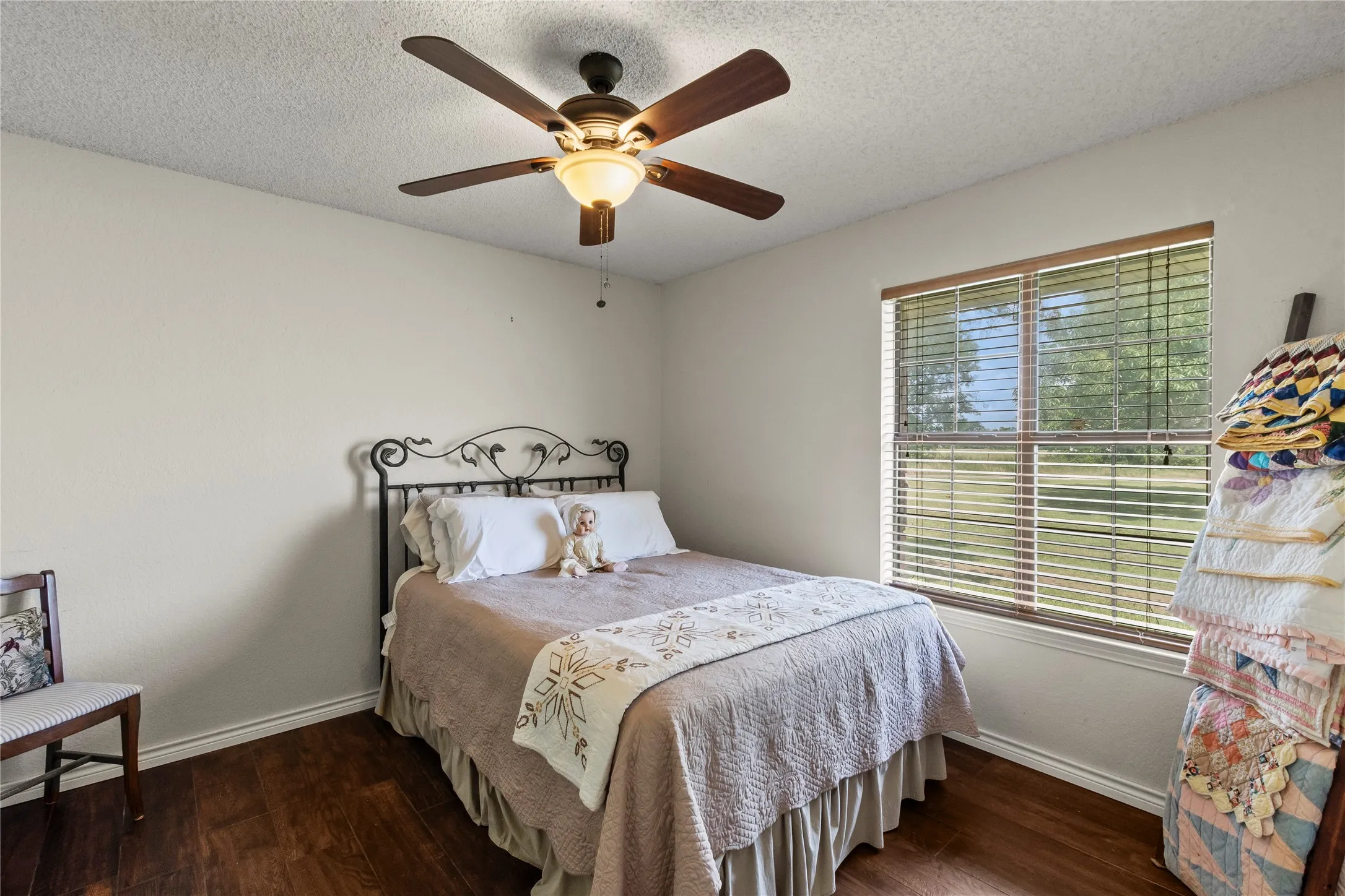 Spacious bedroom featuring wood-finish flooring, a ceiling fan with integrated lighting, and a large window with horizontal blinds