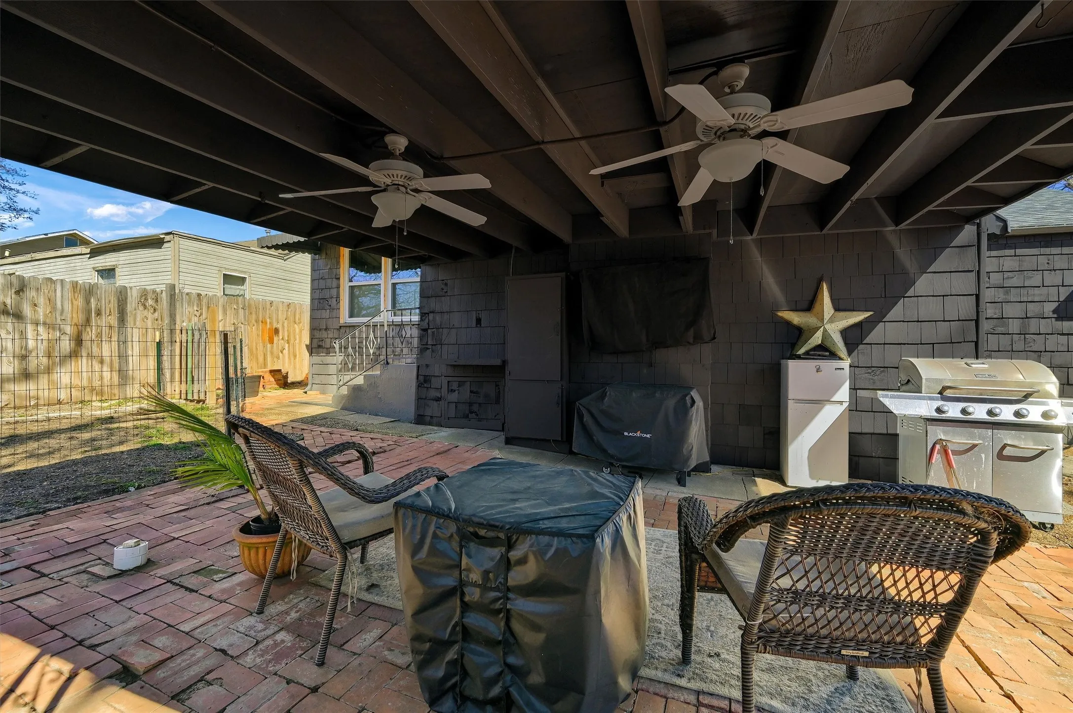 Covered outdoor patio area featuring a brick paver surface, dual ceiling fans, and wood shingle exterior siding