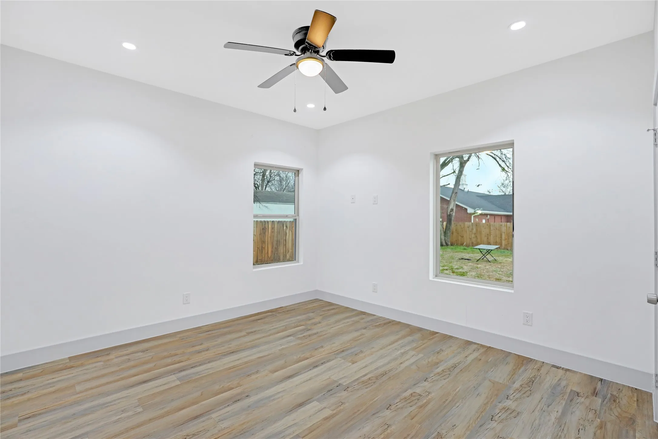 Light-filled room featuring wood-finish flooring, recessed lighting, and a modern ceiling fan