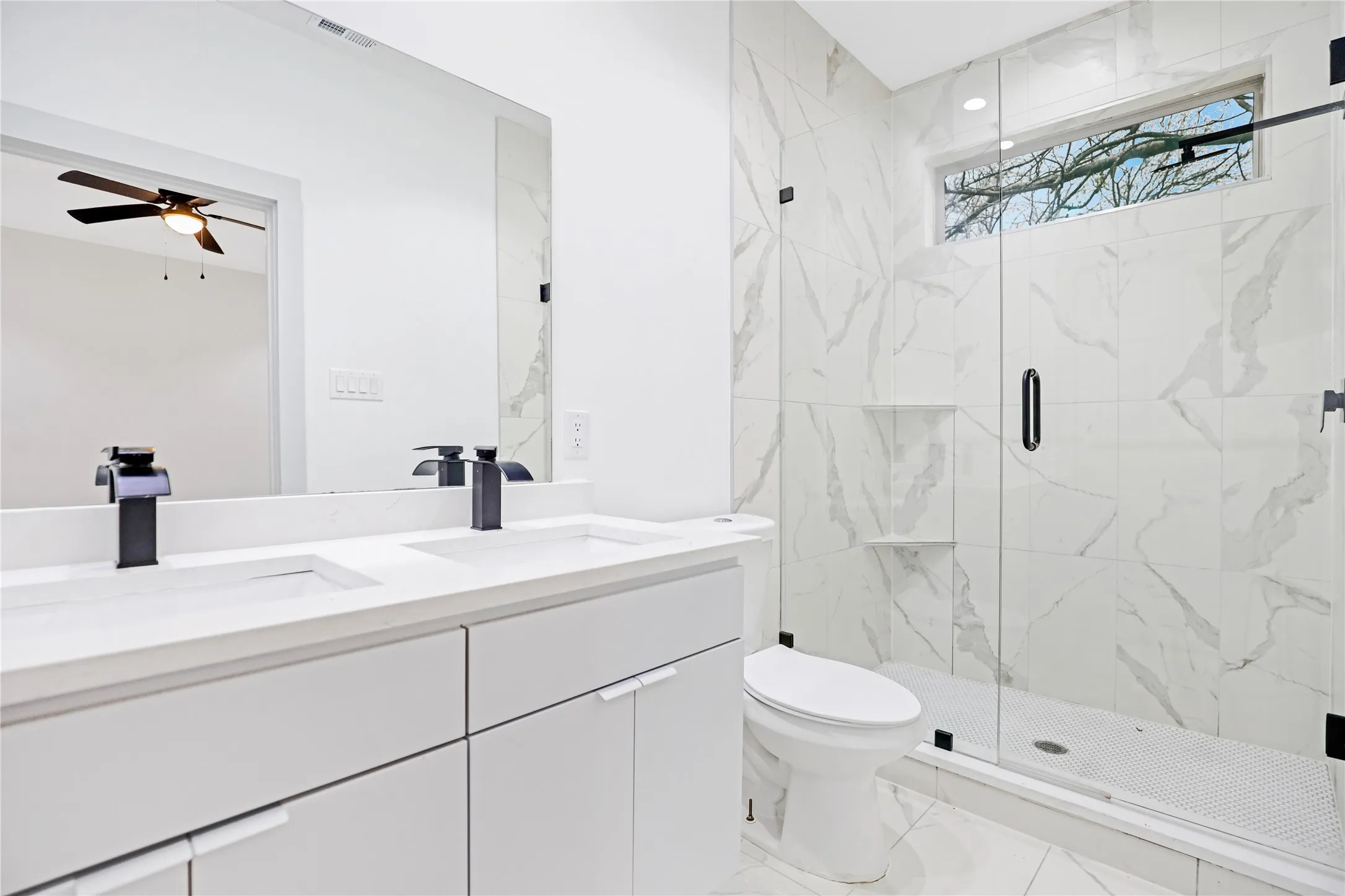 Contemporary bathroom featuring a frameless glass shower enclosure with white marbled tile, a dual vanity with undermount sinks, and matte black fixtures