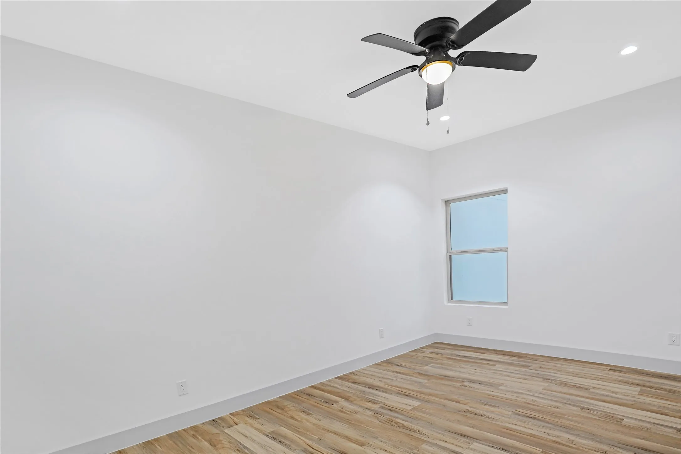 Bright interior space featuring wood-finish flooring, a contemporary ceiling fan with integrated lighting, recessed lighting, a single window, and clean white baseboards
