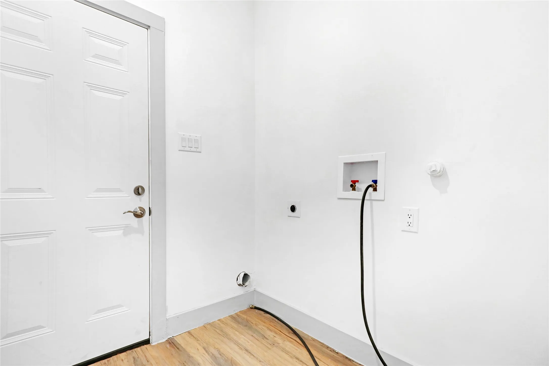 Dedicated laundry area featuring wood-finish flooring, a six-panel door with brushed nickel hardware, and a recessed wall box for washer hookups