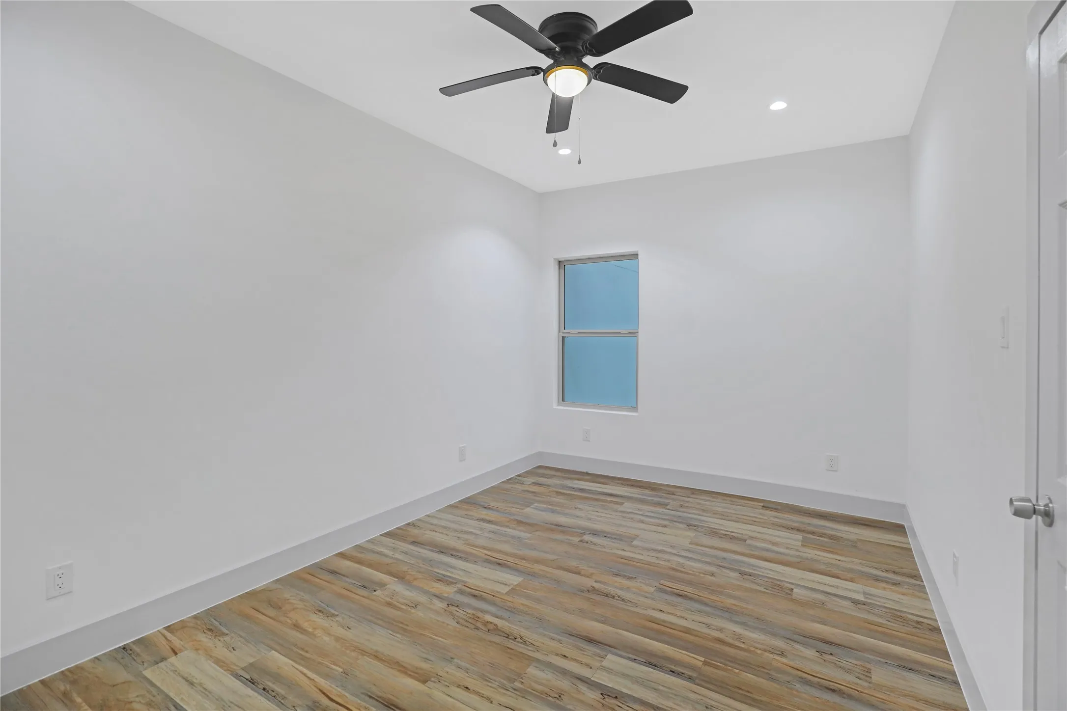 Spacious room featuring wood-finish flooring, a contemporary ceiling fan, recessed lighting, and a window for natural light