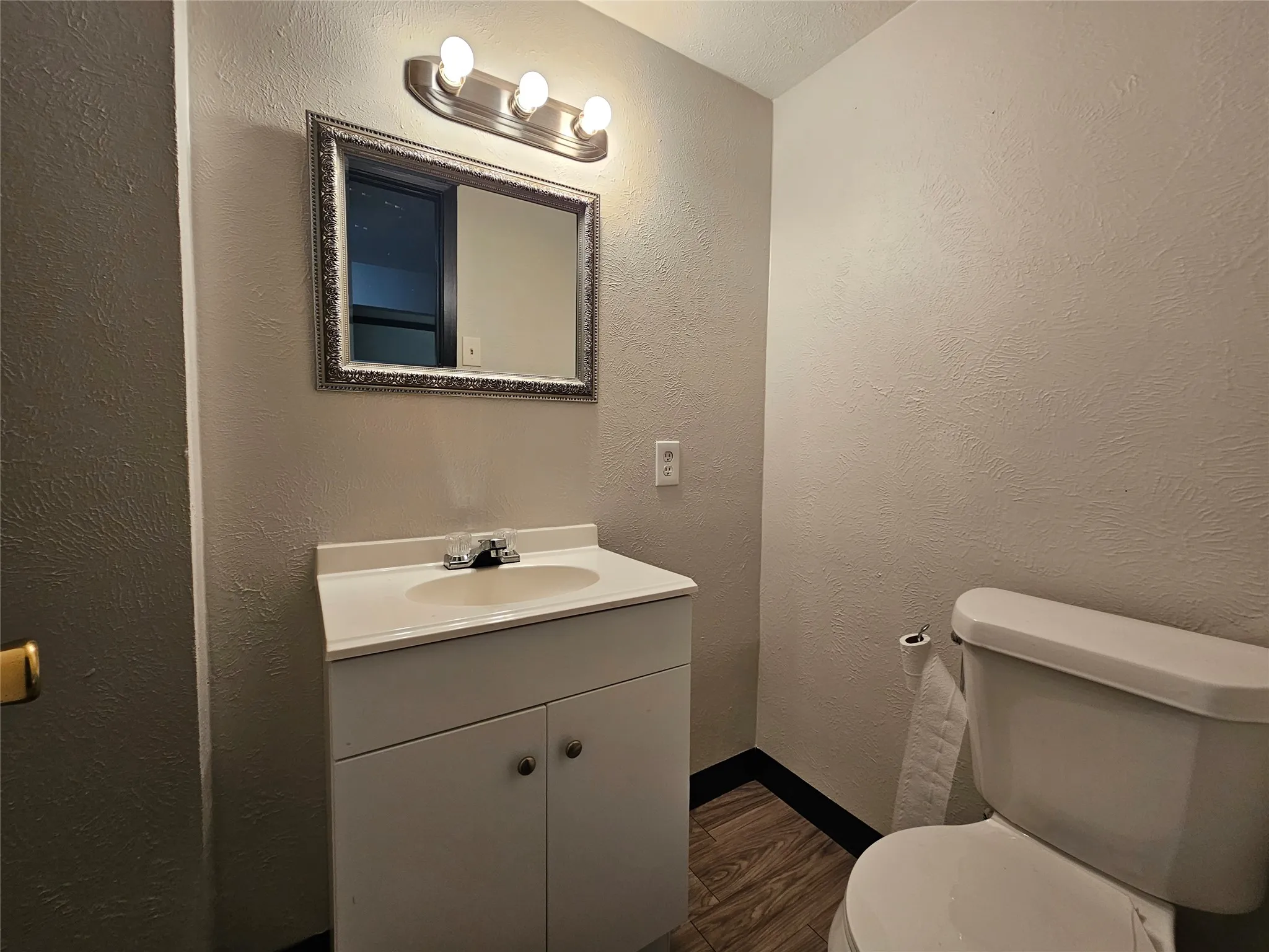 Compact bathroom featuring a white vanity with integrated sink, chrome faucet, and overhead three-bulb vanity light