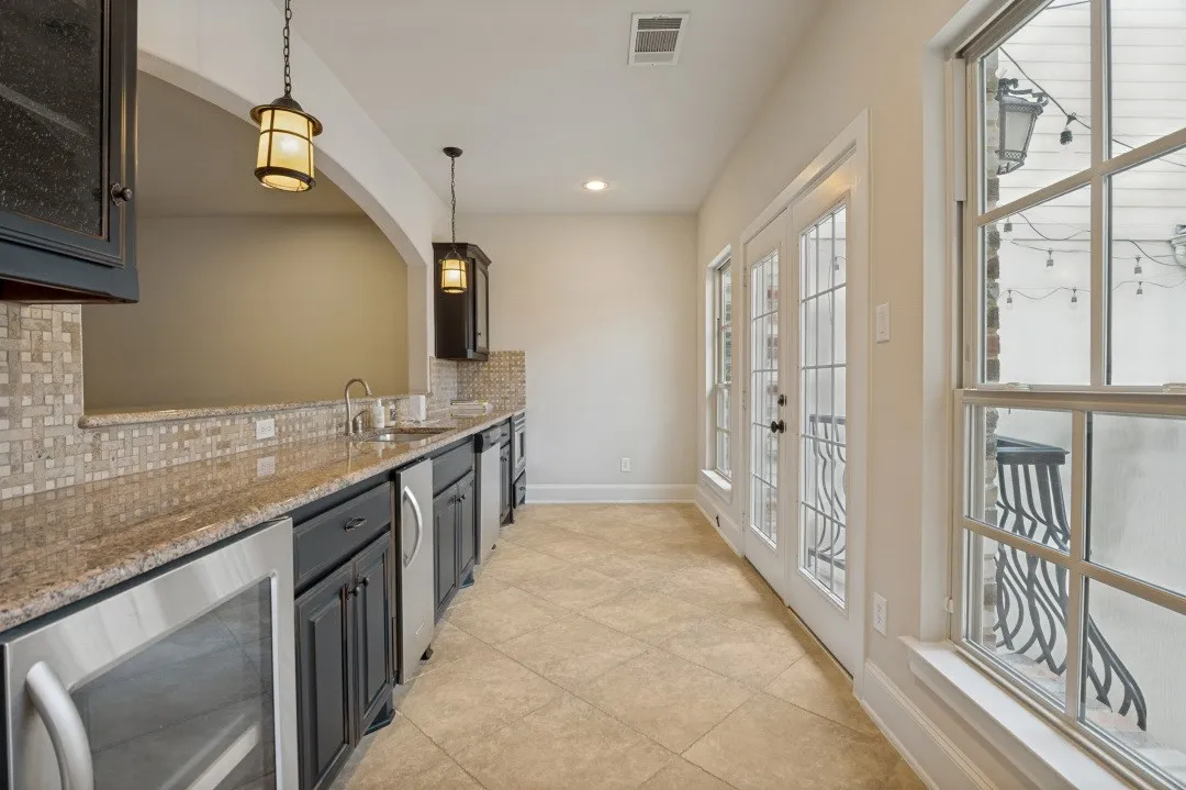 Kitchenette featuring granite countertops, a mosaic tile backsplash, dark wood cabinetry, stainless steel appliances, and tile flooring