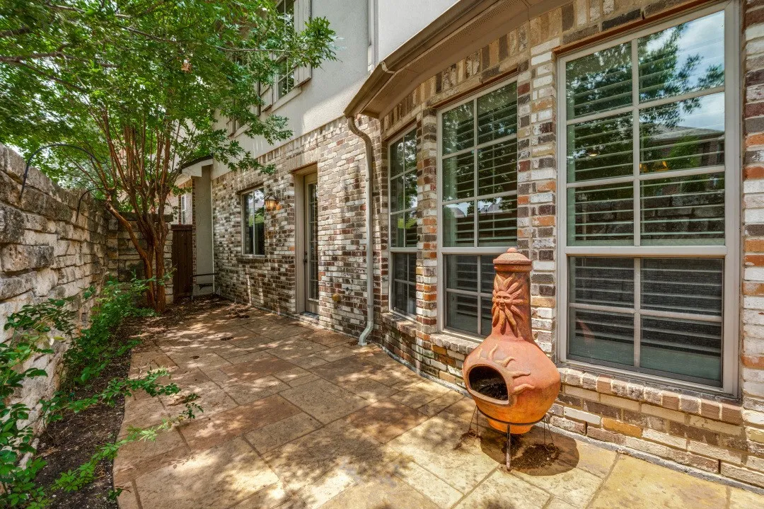 Patio area featuring large stone pavers, a natural stone privacy wall, and brick exterior with multiple windows