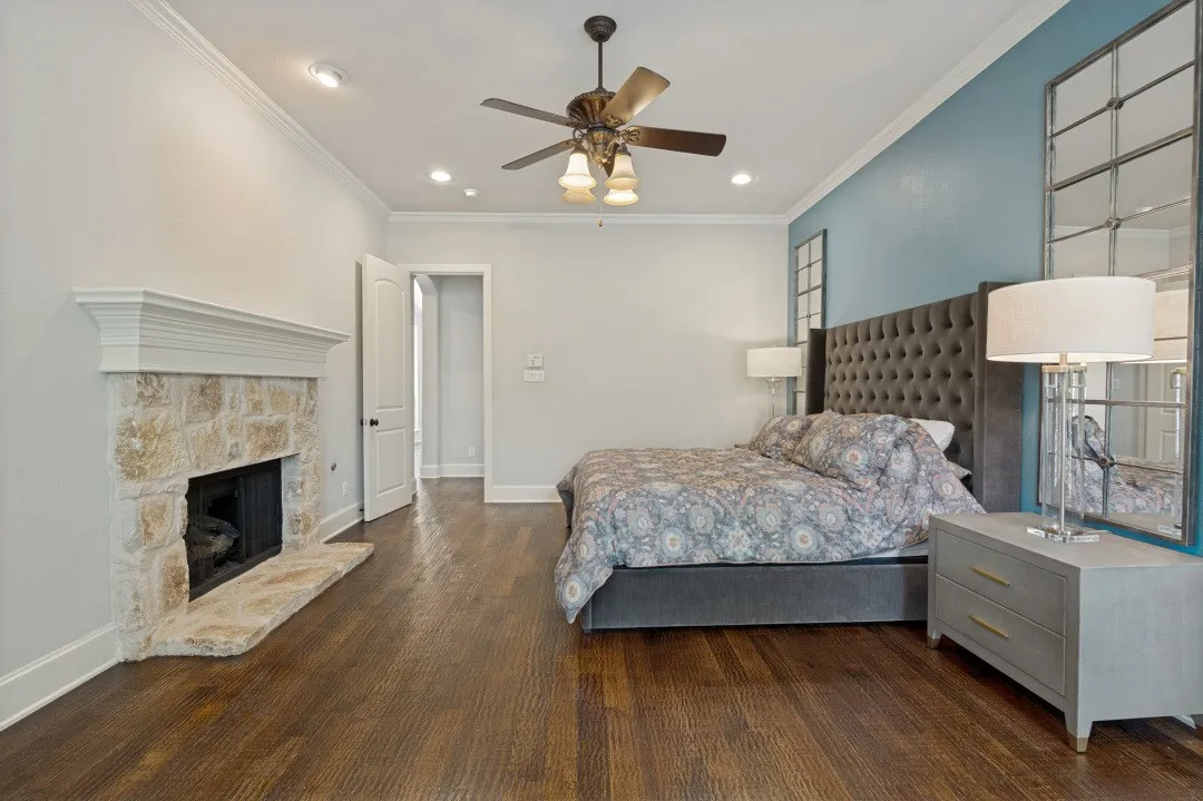 Interior room featuring wood-finish flooring, a stone-faced fireplace with a white mantel, crown molding, and recessed lighting