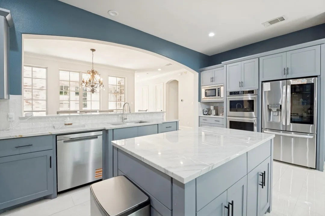 Kitchen featuring light blue cabinetry, stainless steel appliances, a center island with a stone countertop, and a tile backsplash