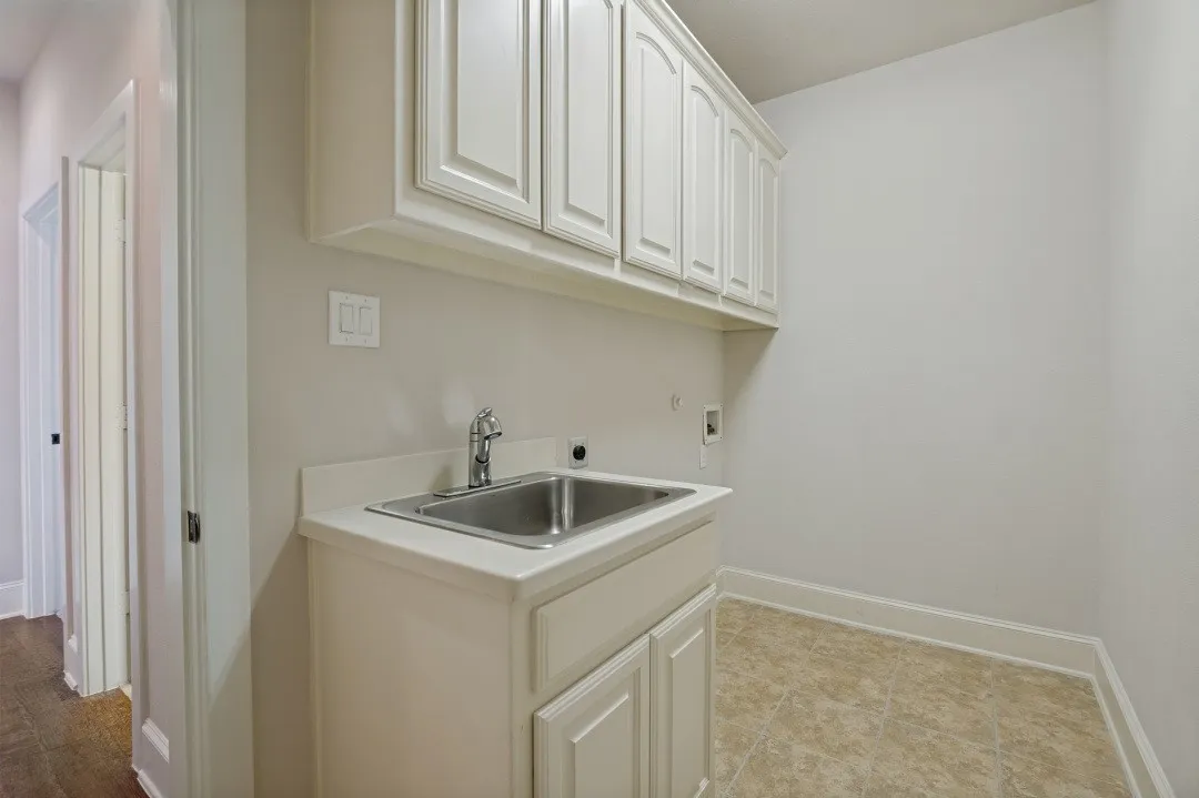 Laundry room featuring white shaker-style cabinetry, a stainless steel utility sink, a white countertop, and tiled flooring