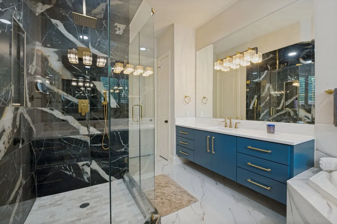 Glass-enclosed shower with black marble-style tile surround and gold-finish fixtures