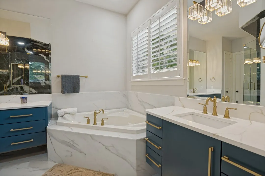 Soaking tub with brass-finish fixtures, surrounded by white marble-look tile