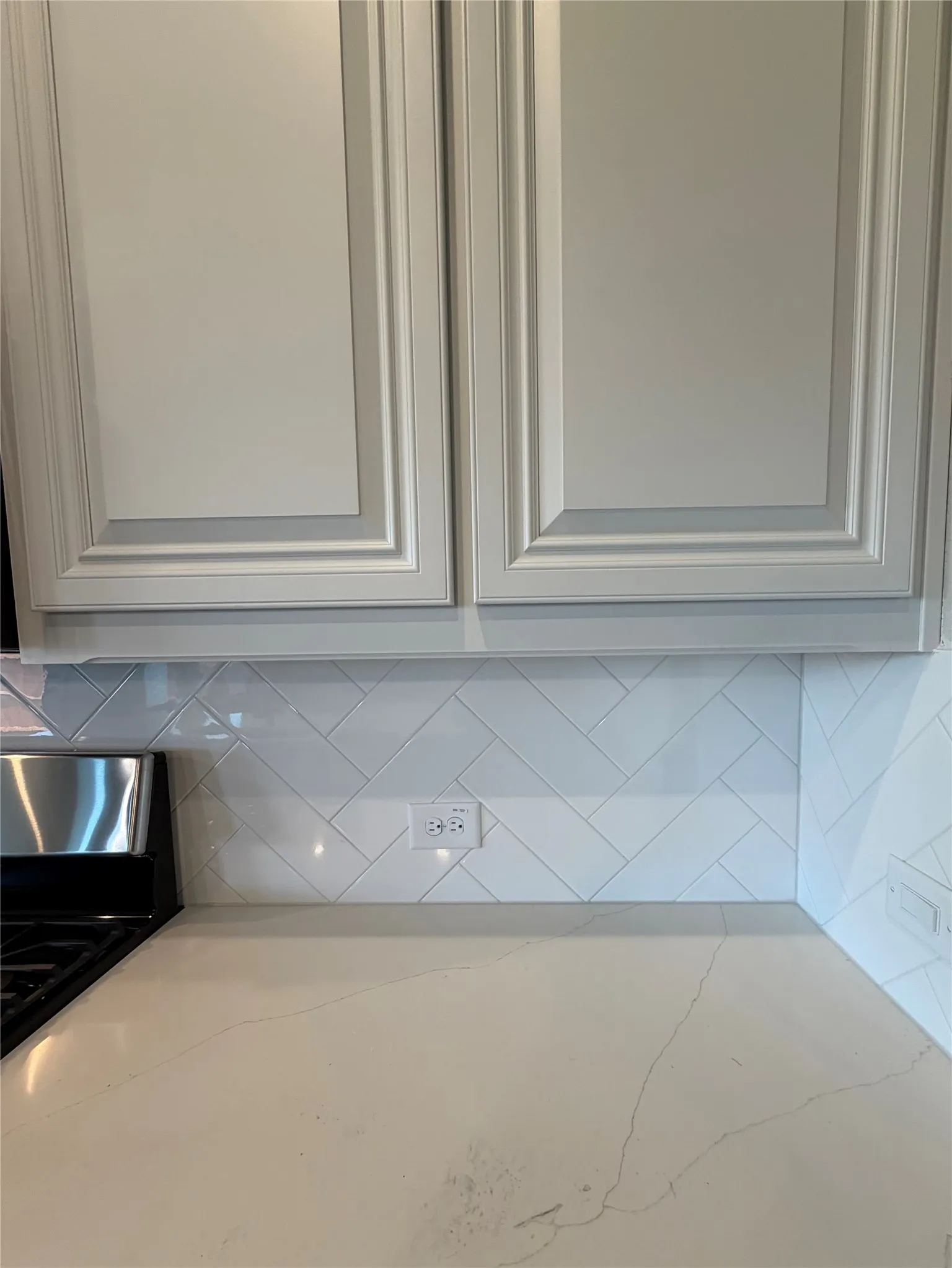 Close-up of White raised-panel cabinets, Lincoln quartz, and white tile in a herringbone pattern.