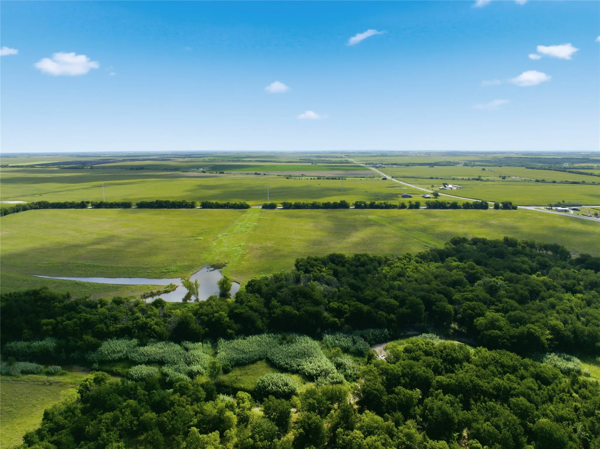 Expansive green landscape featuring a natural water body, dense tree lines, and distant open fields