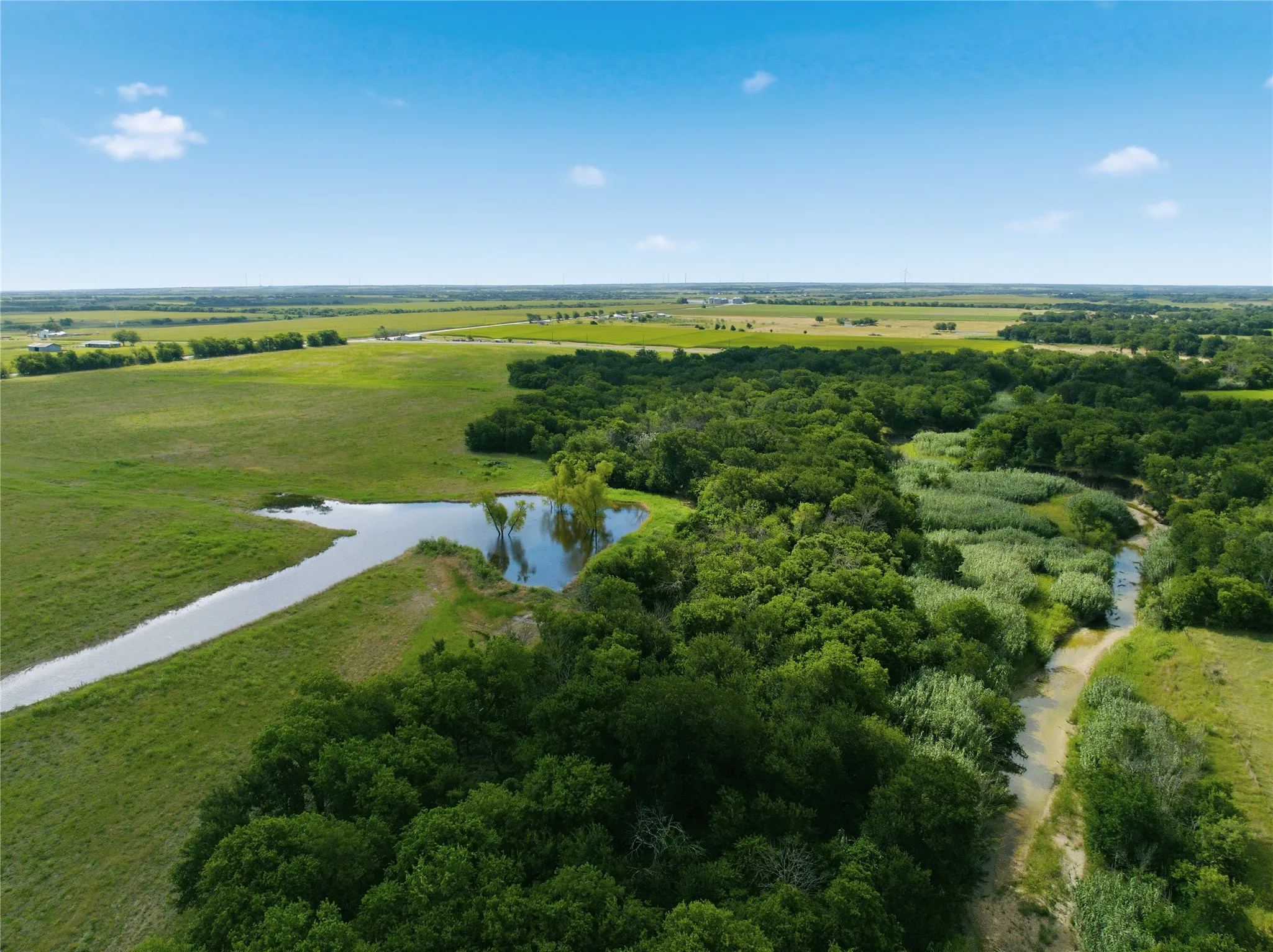 Expansive property featuring a tranquil pond, winding creek, and varied terrain with mature trees and open grasslands