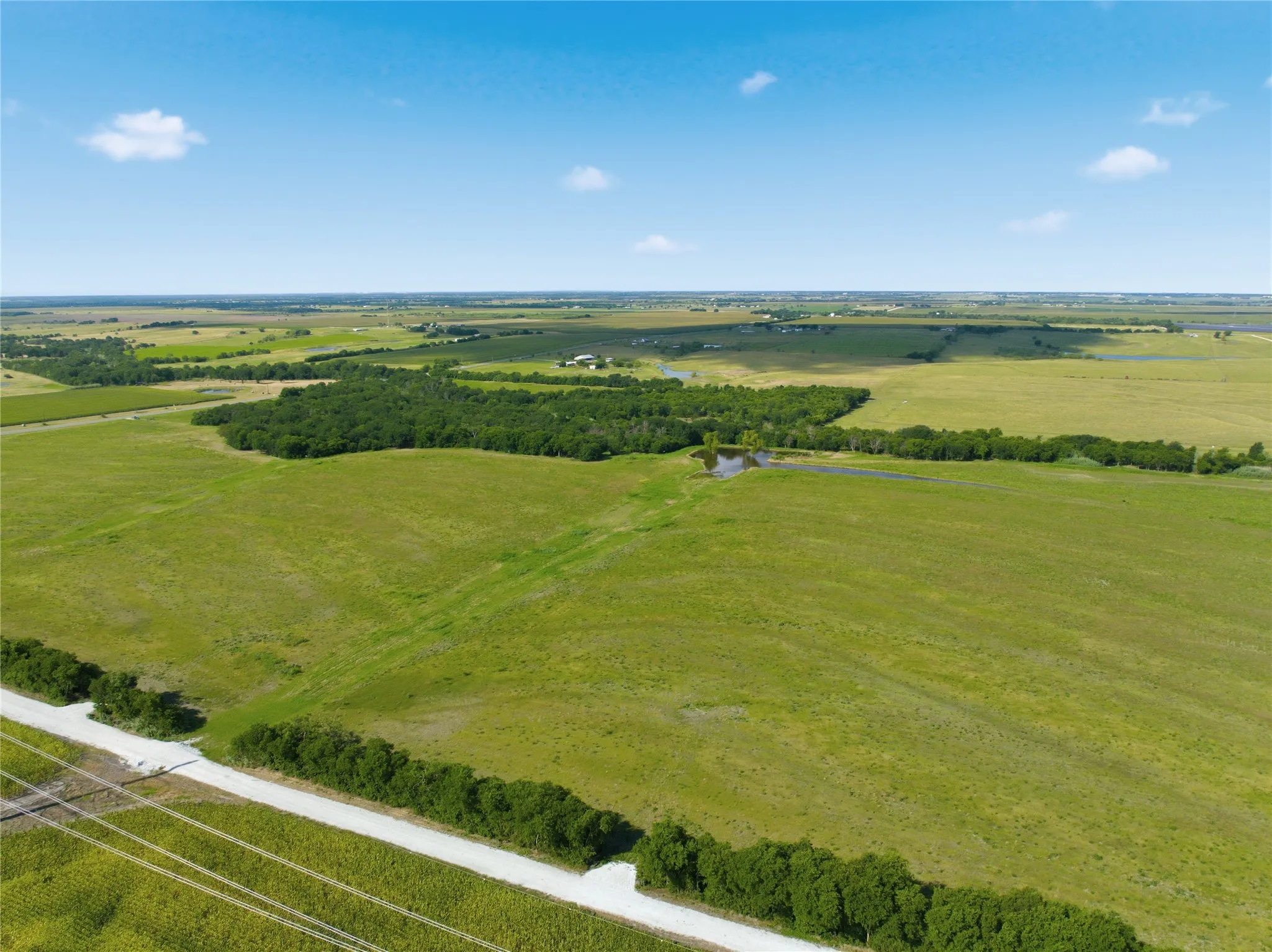 Expansive rural landscape featuring vast open fields, natural tree lines, and a visible pond