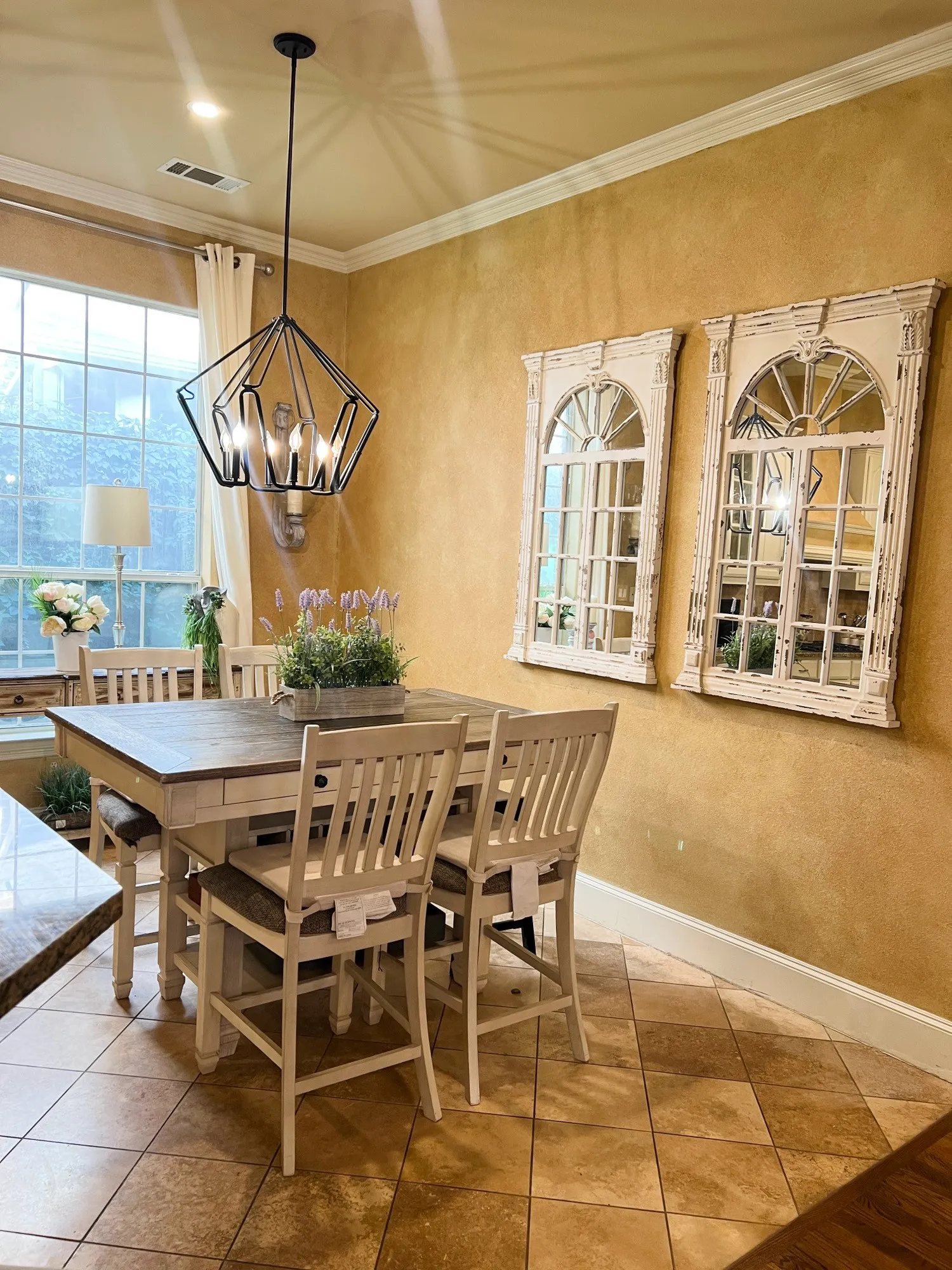 Dining area featuring a contemporary geometric pendant light fixture, large windows with white trim, crown molding, and light-toned floor tiling